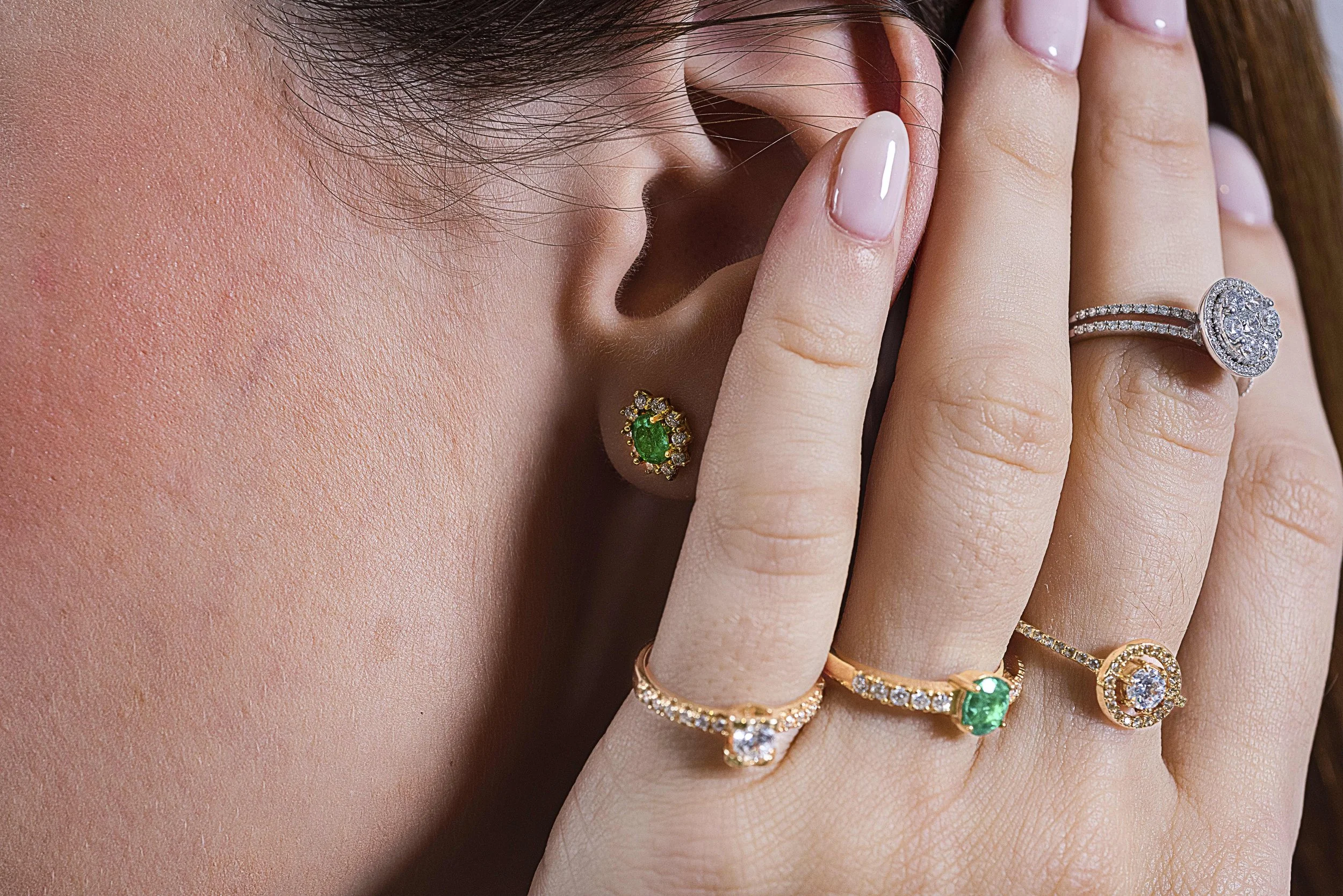 Muñeca con varios anillos y una bolita en el oído con piedras preciosas, cerca del rostro y del cabello.
