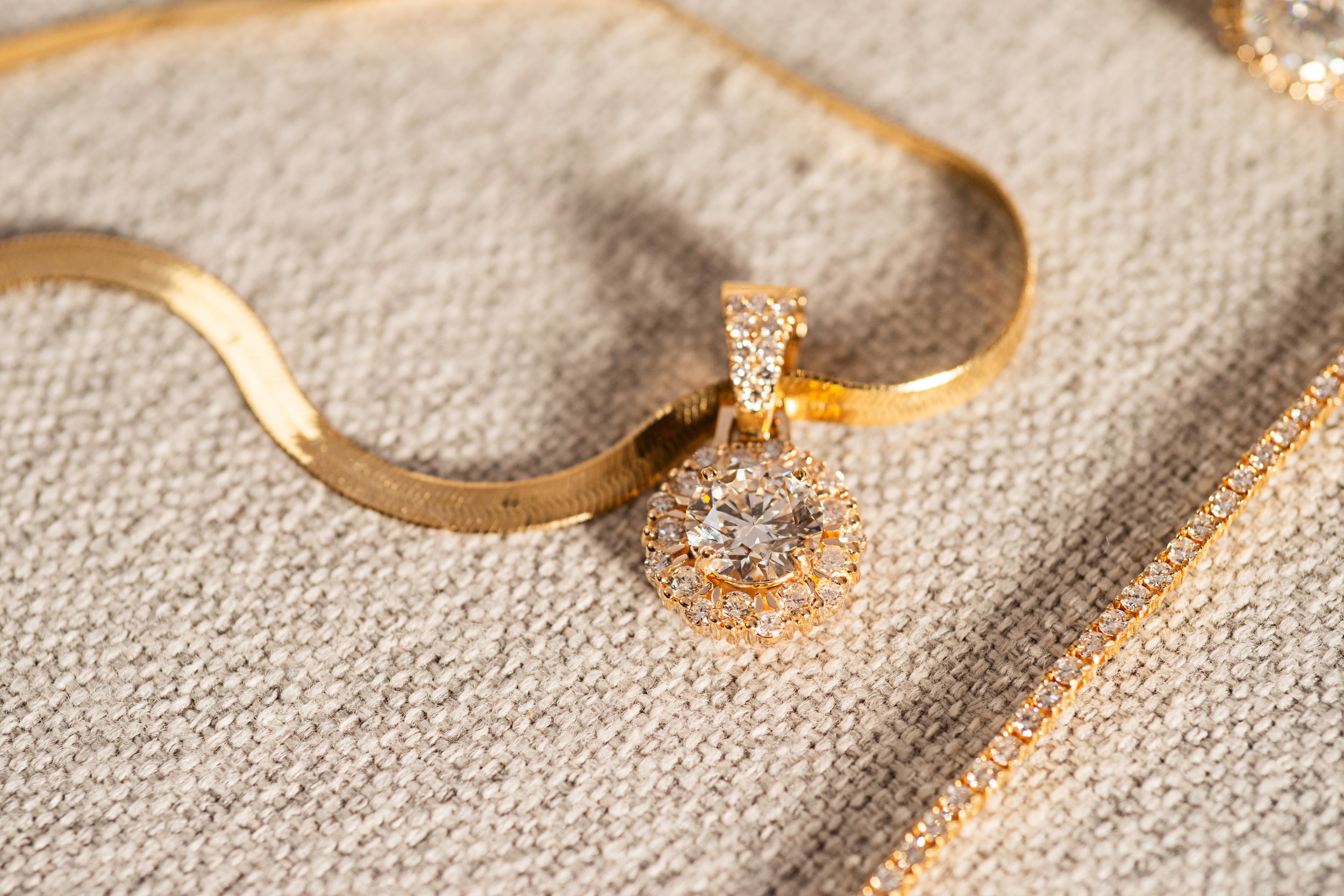 Collar, reloj y colgante de oro con piedras brillantes sobre tela de color beige