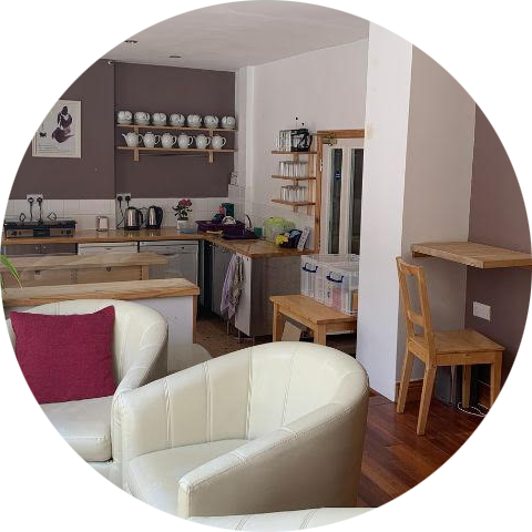 Cozy open-concept  space, a kitchen area with wooden shelves and white dishware, and a small wooden dining table with chair.