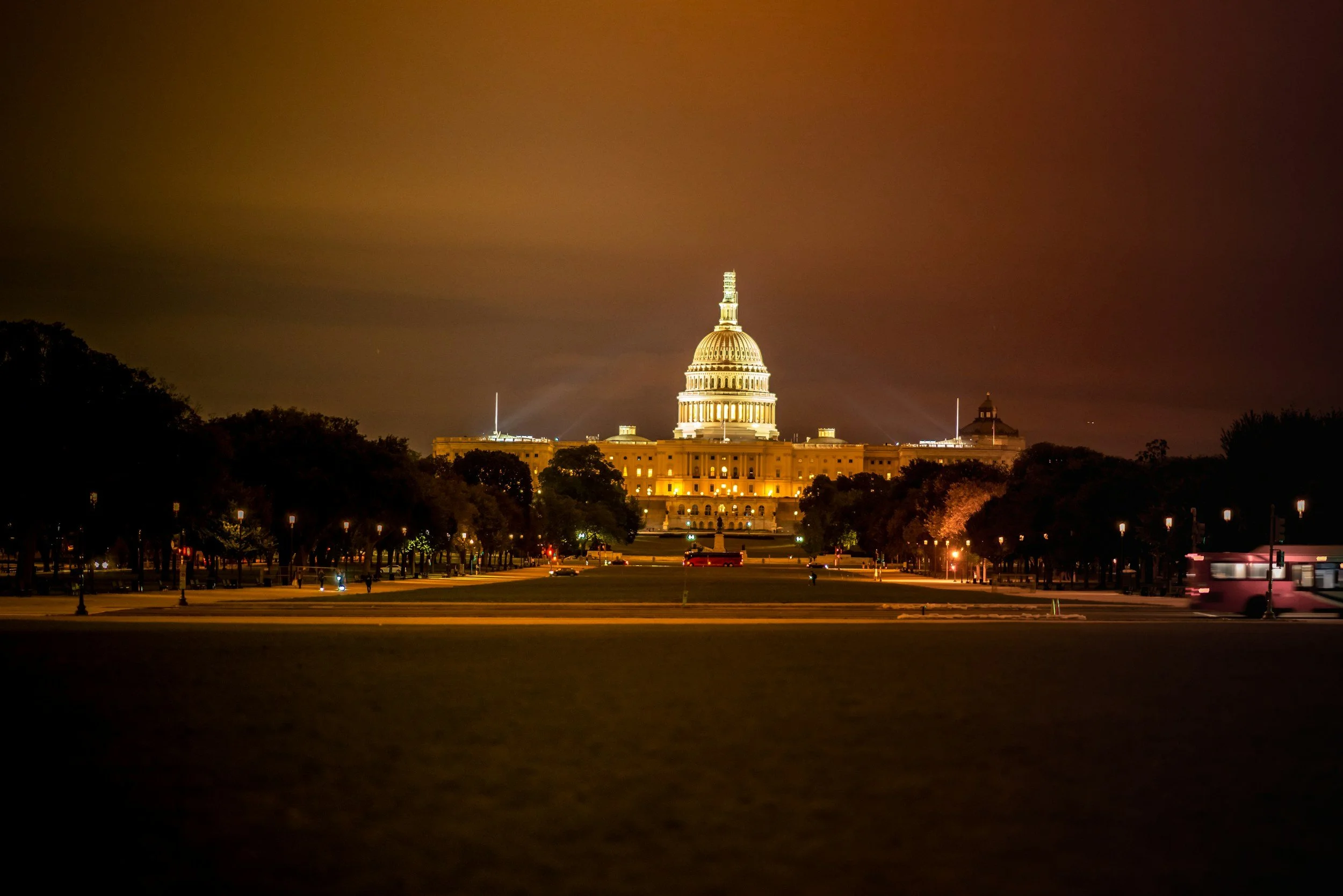 Night view of the United States Capitol building illuminated, with a cloudy sky and trees in the foreground.