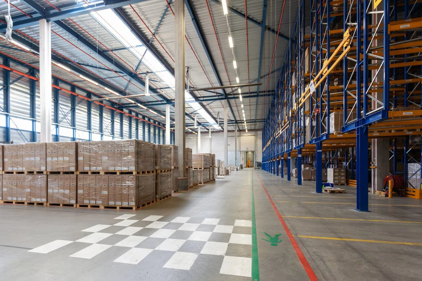 Empty warehouse with pallet stacks on the left and empty shelving units on the right, overcast lighting