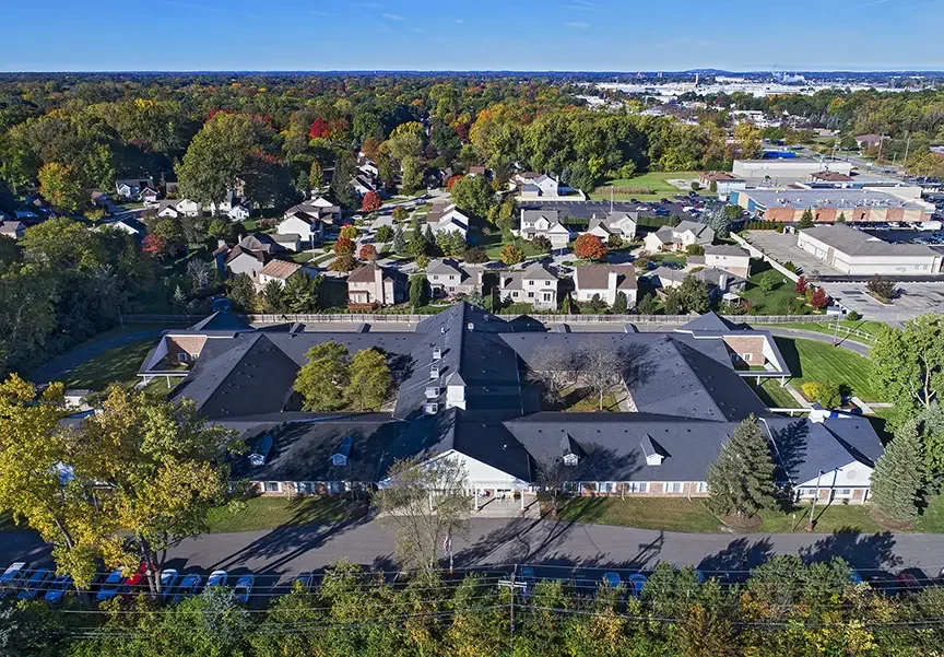 Aerial view of a residential area with houses, trees, and a large building complex surrounded by greenery.