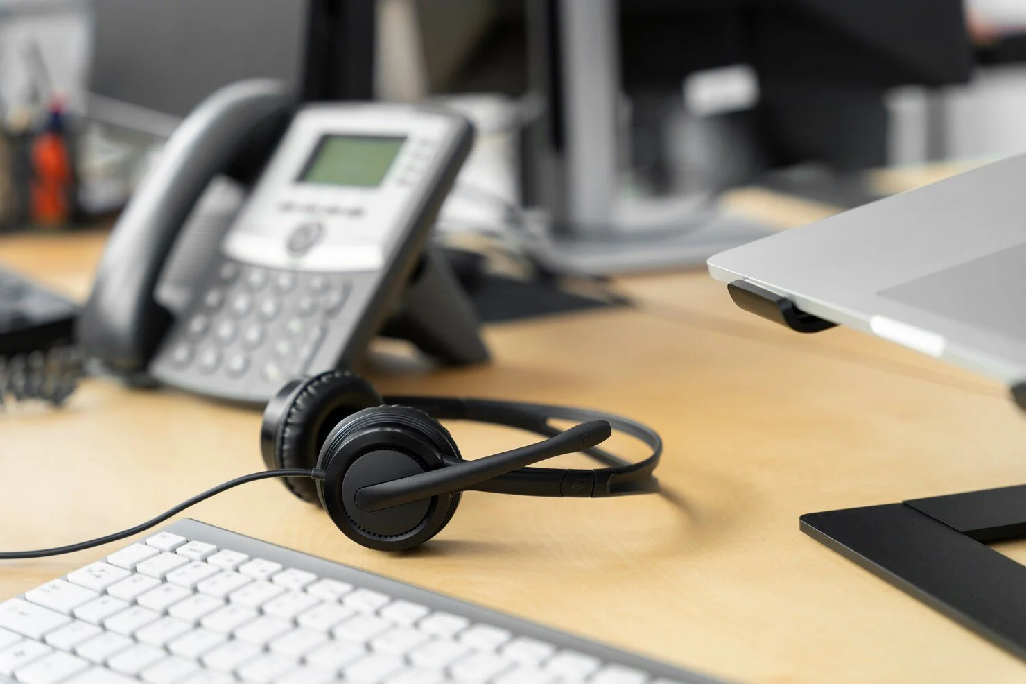 Office desk with a wireless headset, a landline phone, a wireless keyboard, and a computer monitor.
