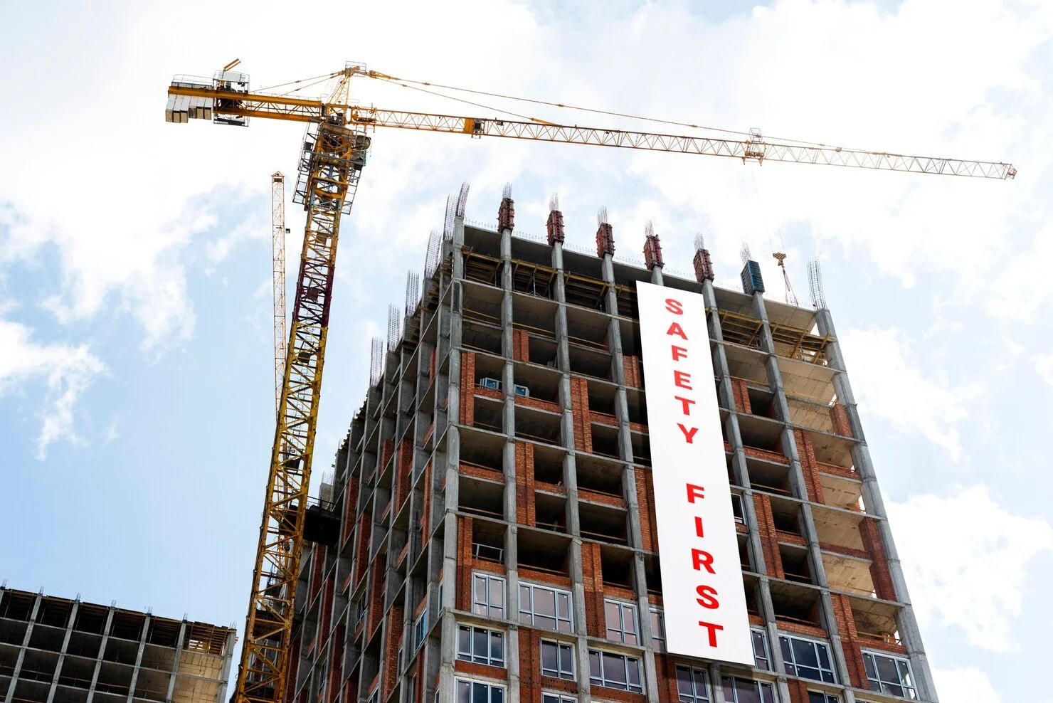 A tall building under construction with a crane next to it and a large vertical sign that reads 'SAFETY FIRST' on the front of the building.