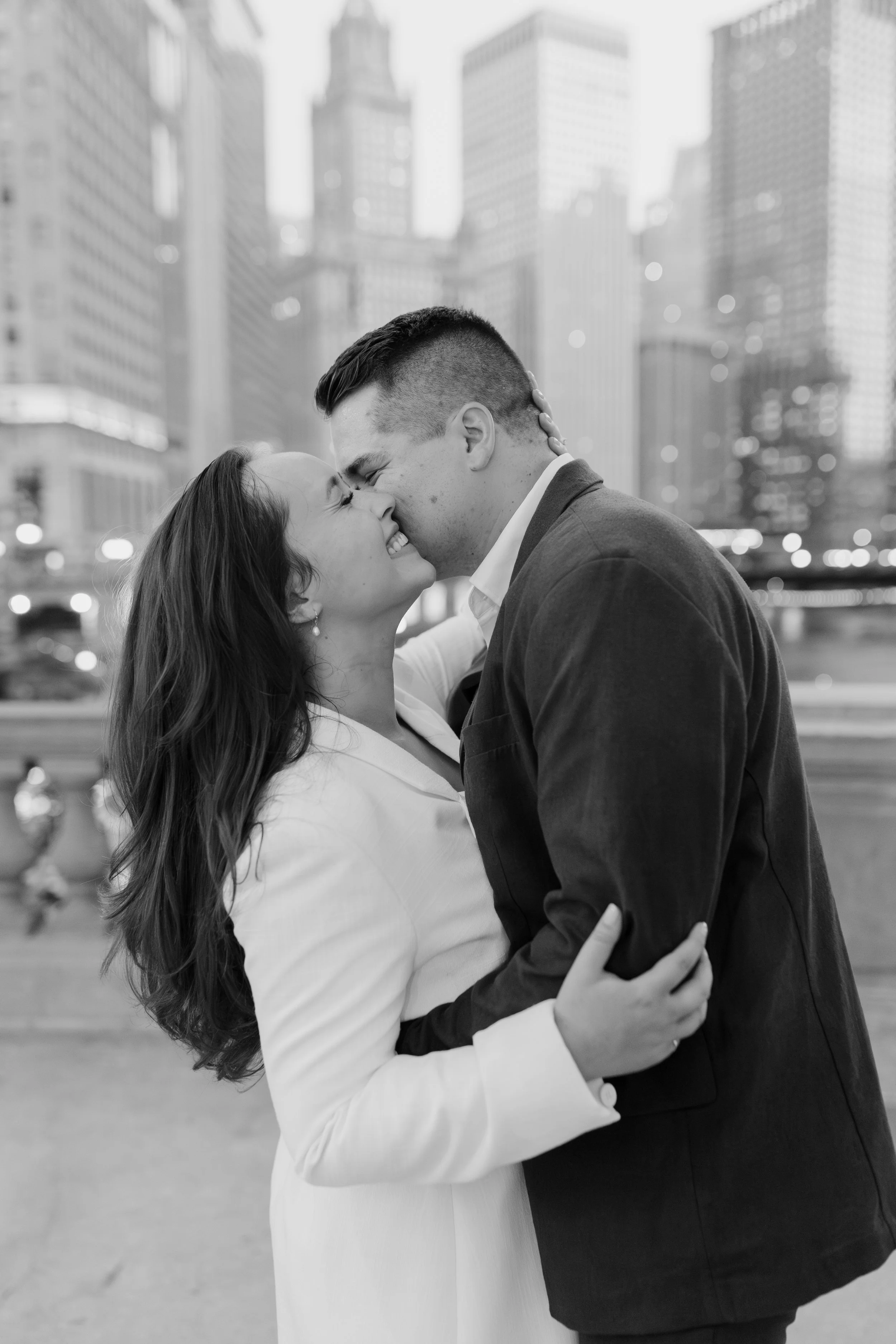 A couple sharing an intimate moment, smiling and about to kiss in an urban setting, in black and white.