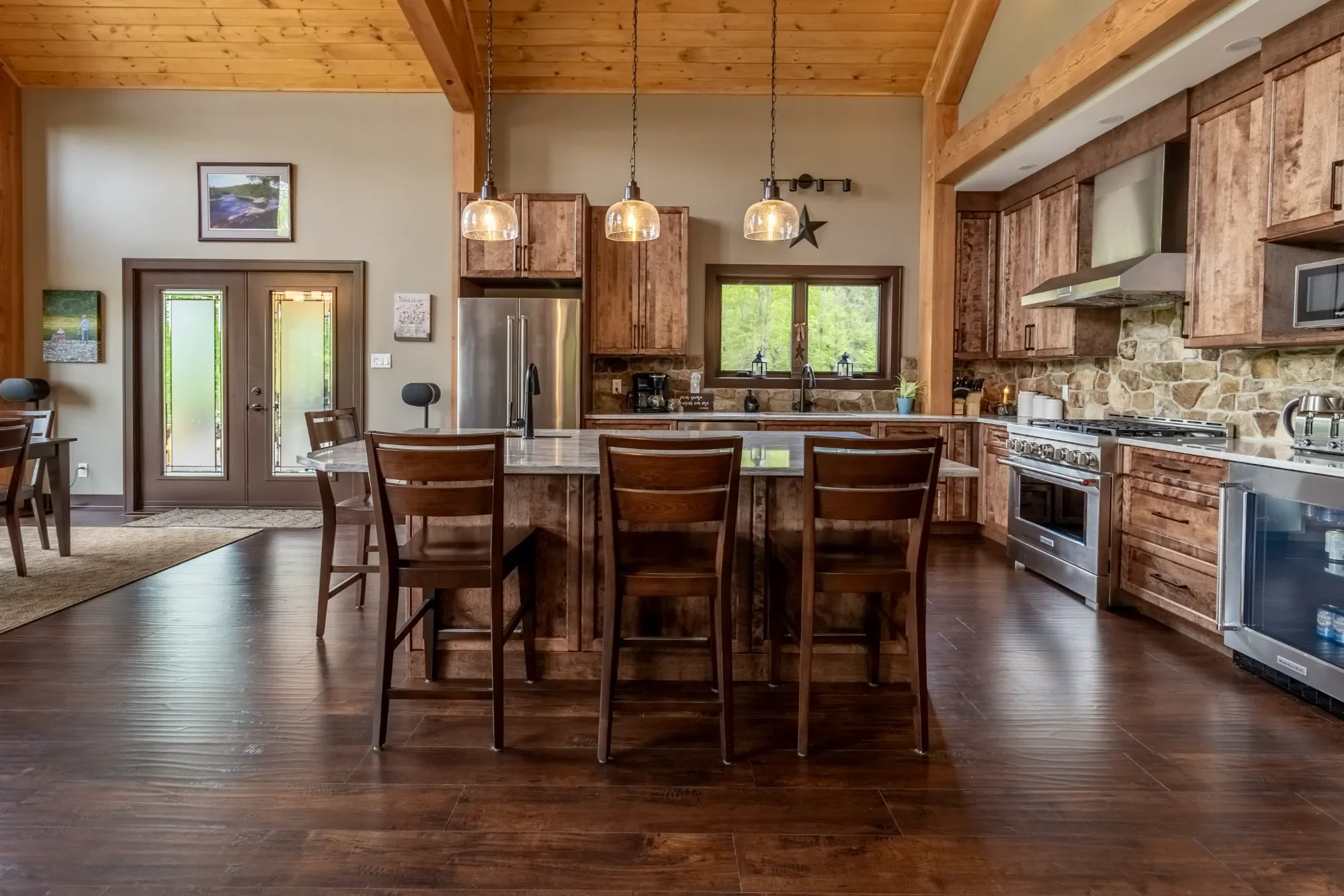 Kitchen with wooden cabinets, an island with bar stools, stainless steel appliances, stone backsplash, and pendant lighting.