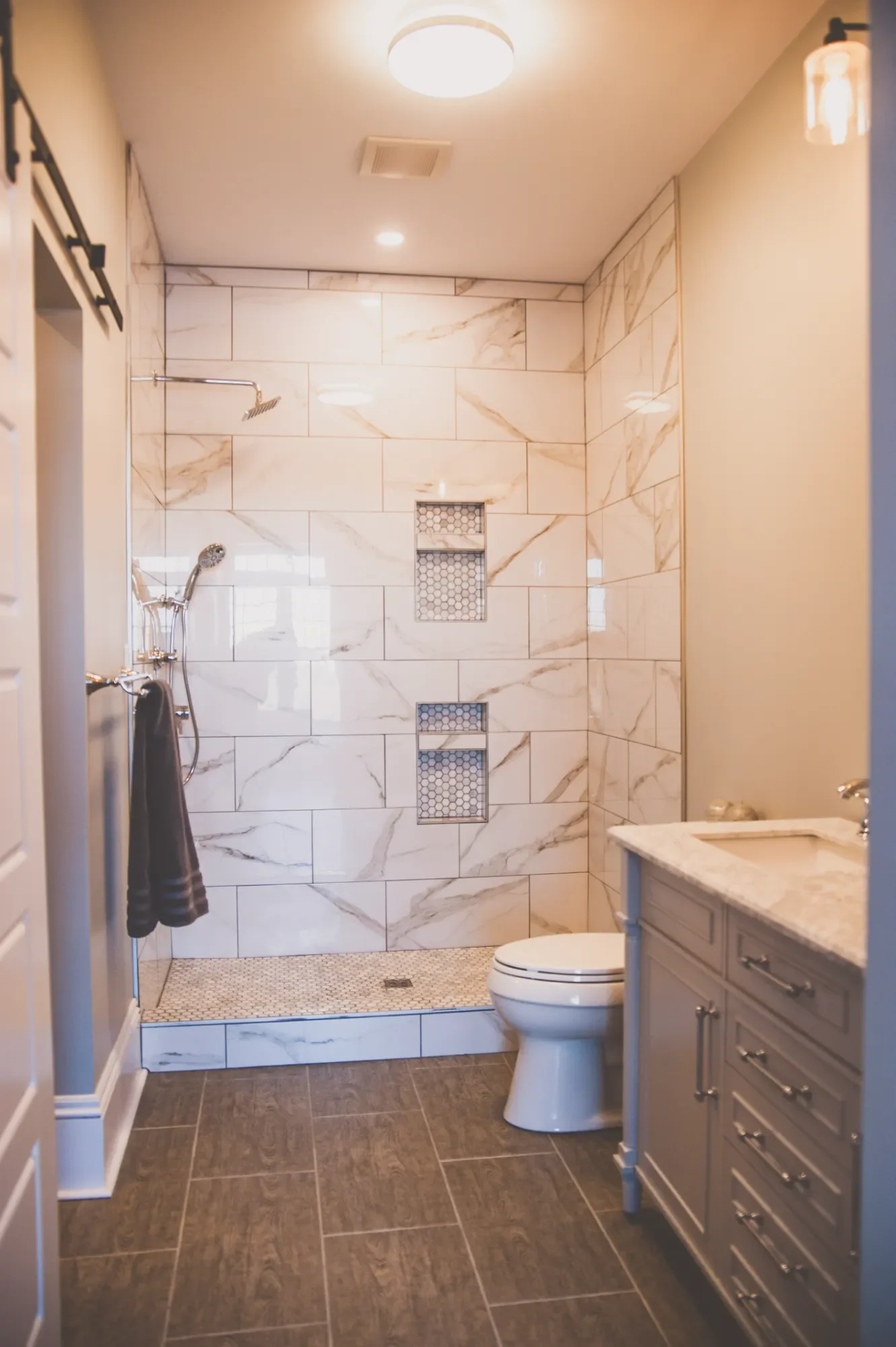 Bathroom with walk-in shower, marble tiles, built-in shower niches, toilet, and gray vanity with countertop.
