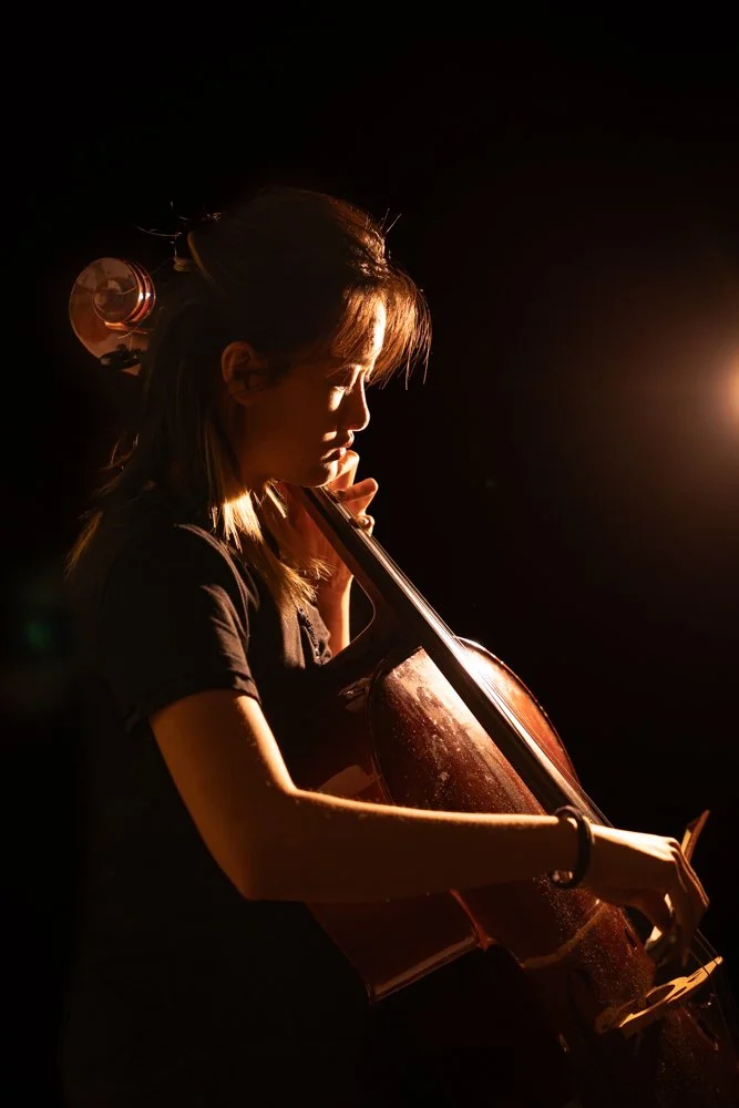 Low-light portrait of a young musician holding a cello, focused and introspective mood