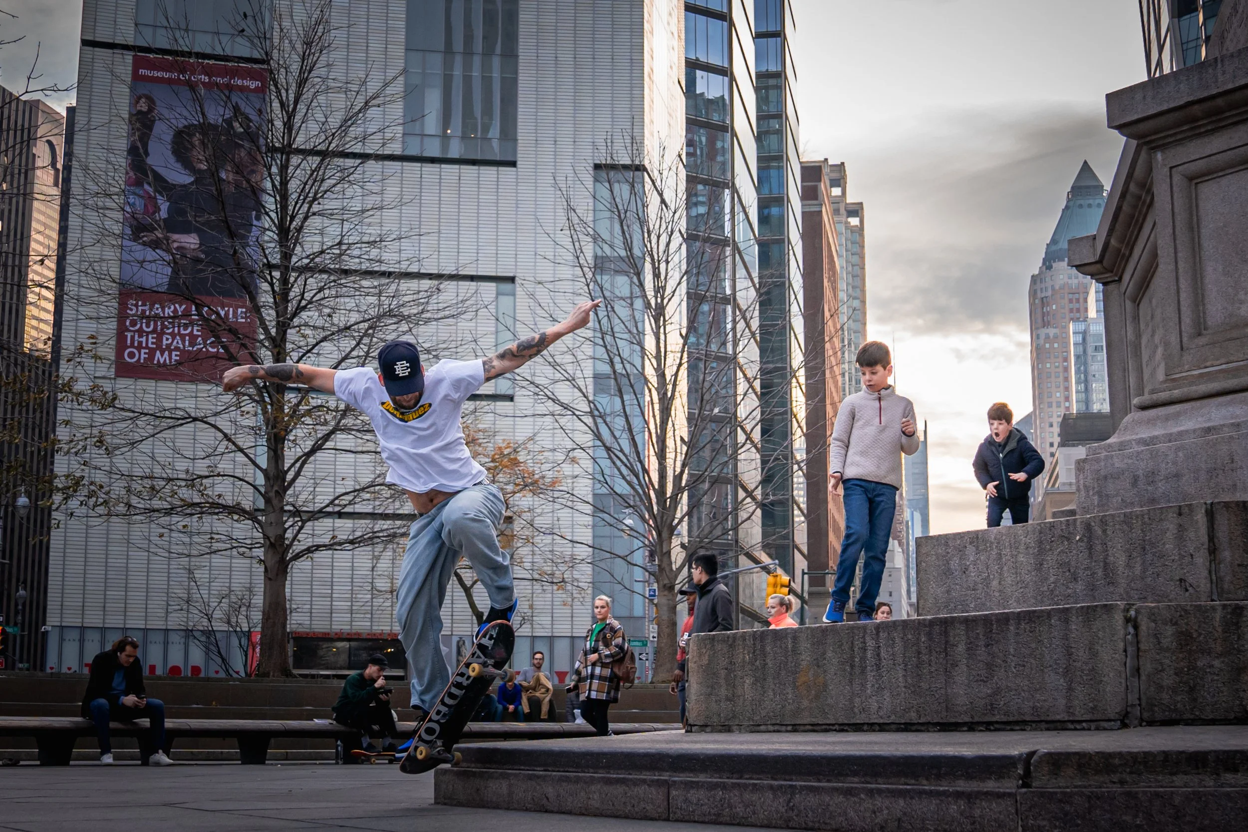 A skateboarder jumping near a public monument in an urban plaza