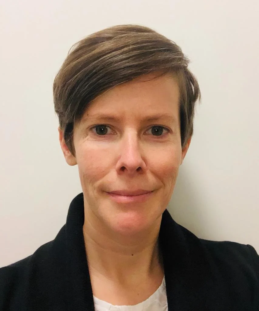 Nahaufnahme einer Frau mit kurzen braunen Haaren, die vor einem weißen Hintergrund steht.