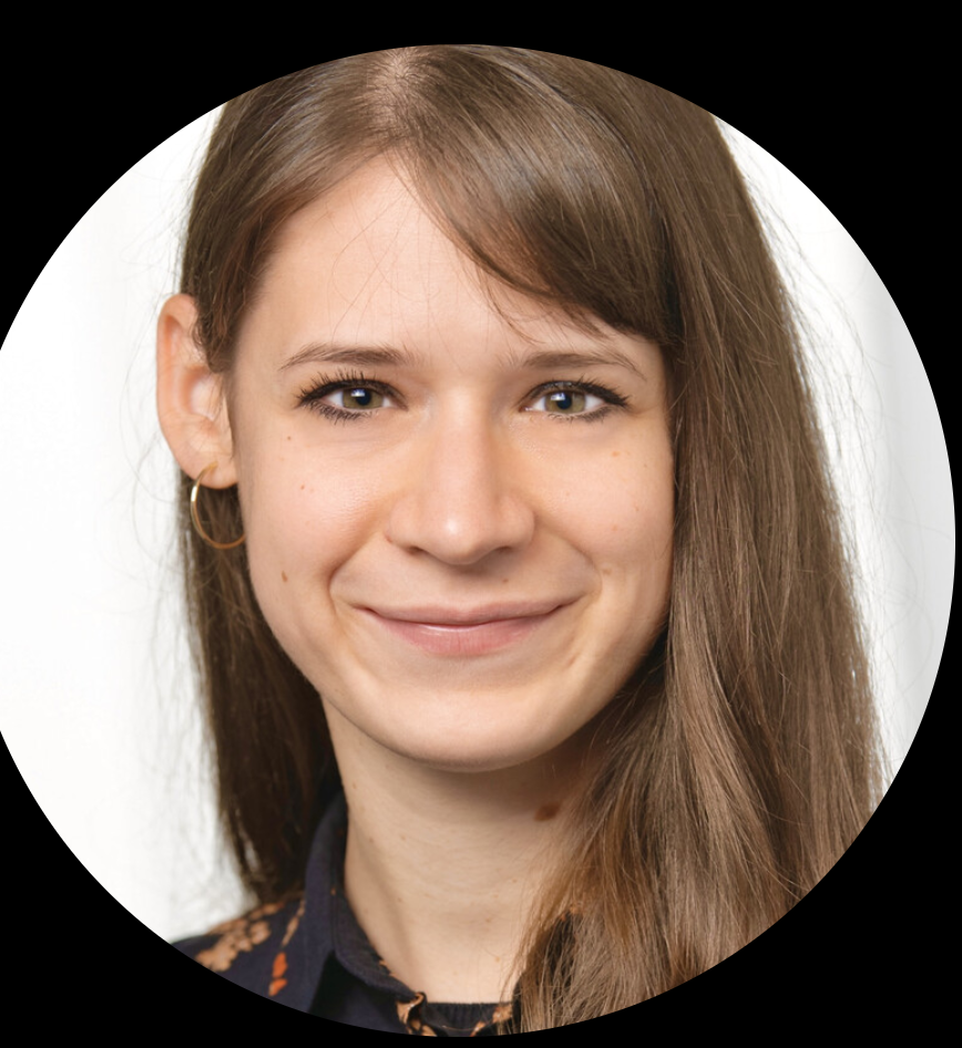 Porträt einer jungen Frau mit langen braunen Haaren, goldenen Haargeldern, einem schwarzen Top mit Mustern, vor weißem Hintergrund.