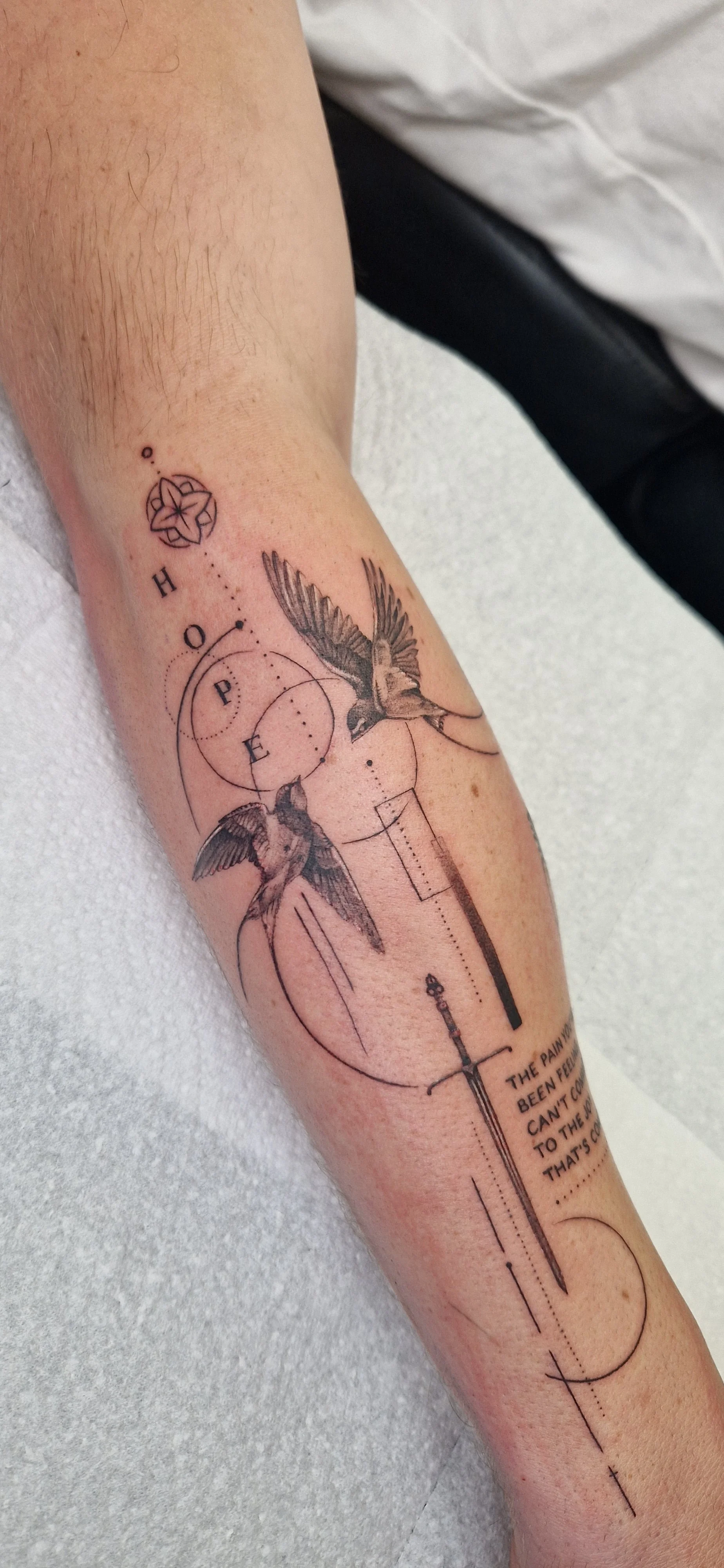 Fine line, micro-realism concept tattoo of two swallows, geometric shapes, and lines on a person's forearm.