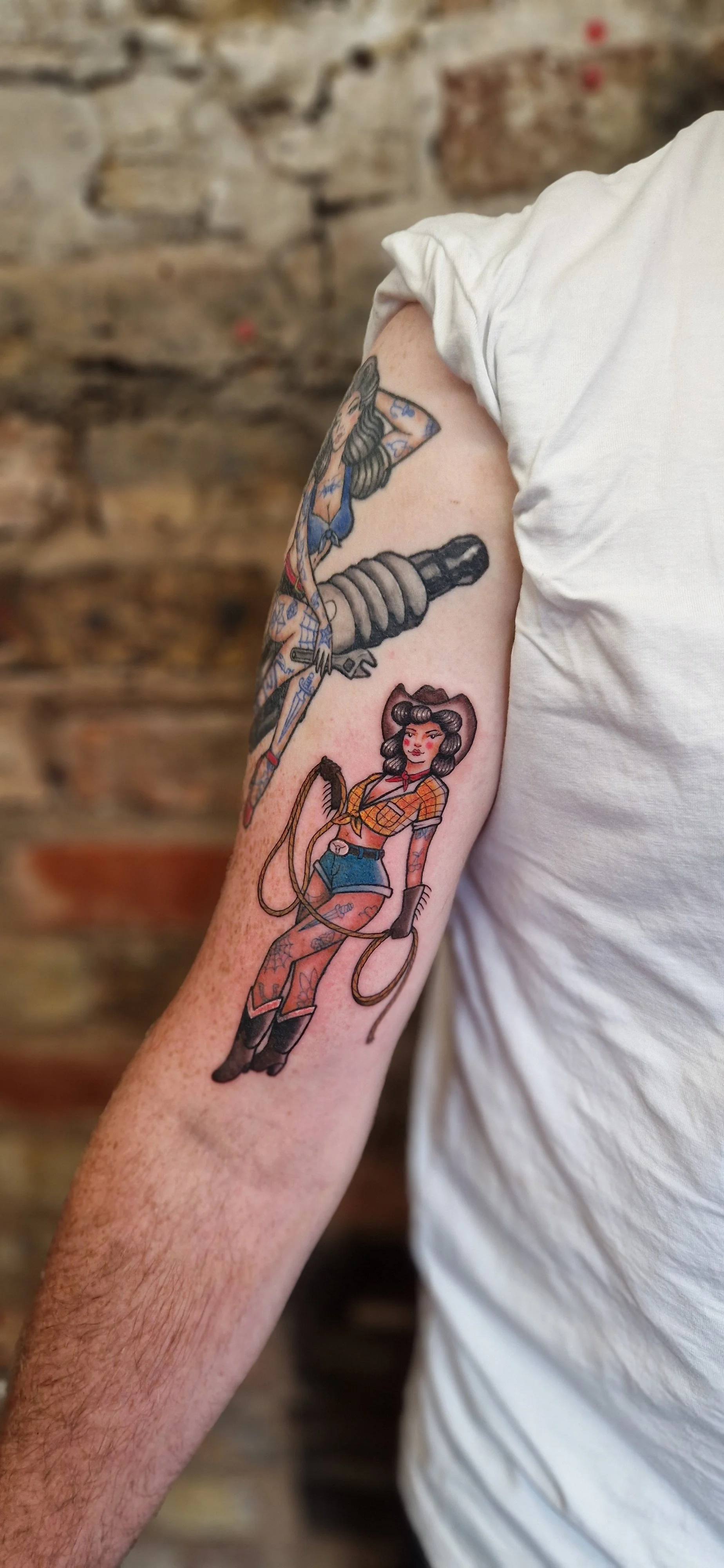 Bold pin-up style full colour tattoo of a cowgirl with vintage hair, and cowboy boots, holding a lasso.