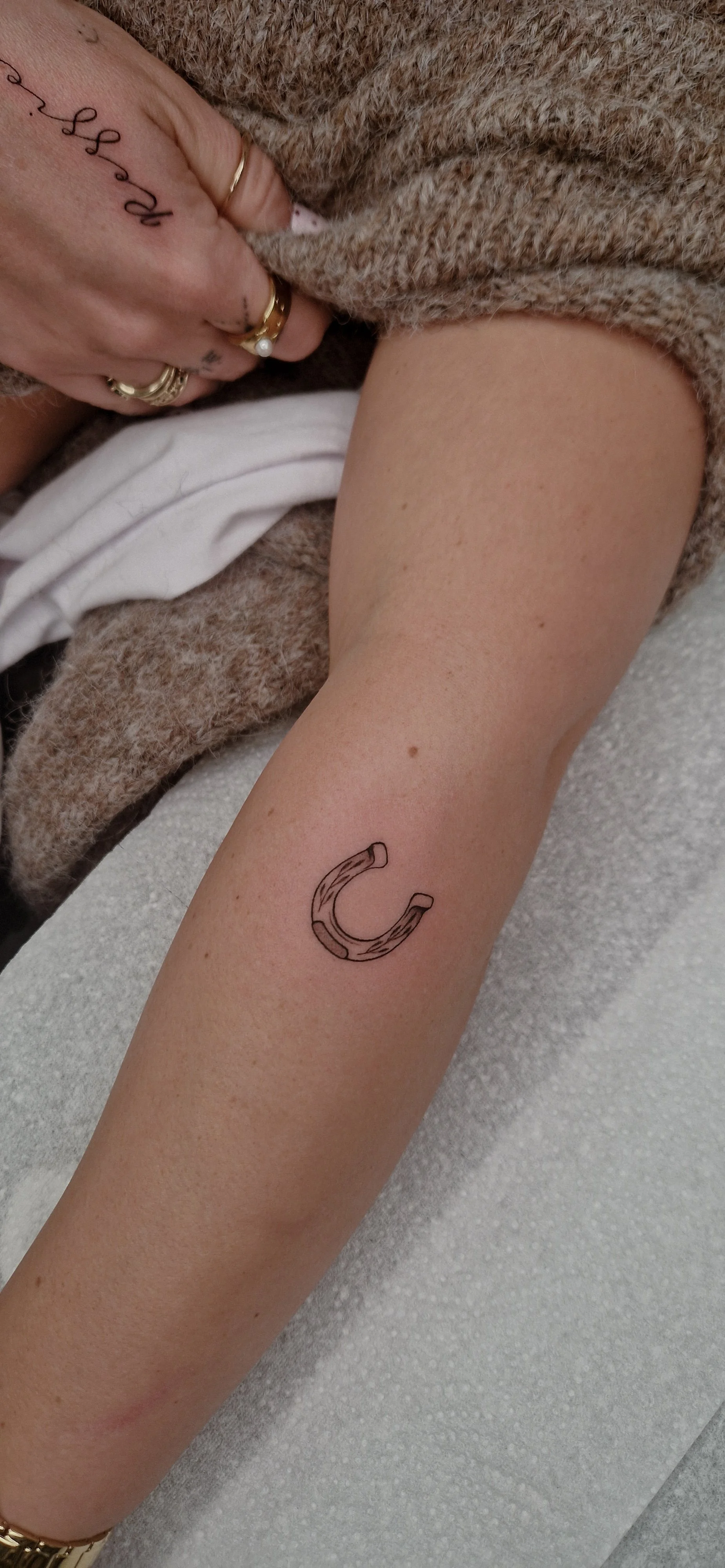 A person's forearm with a small fine line tattoo of a horseshoe.
