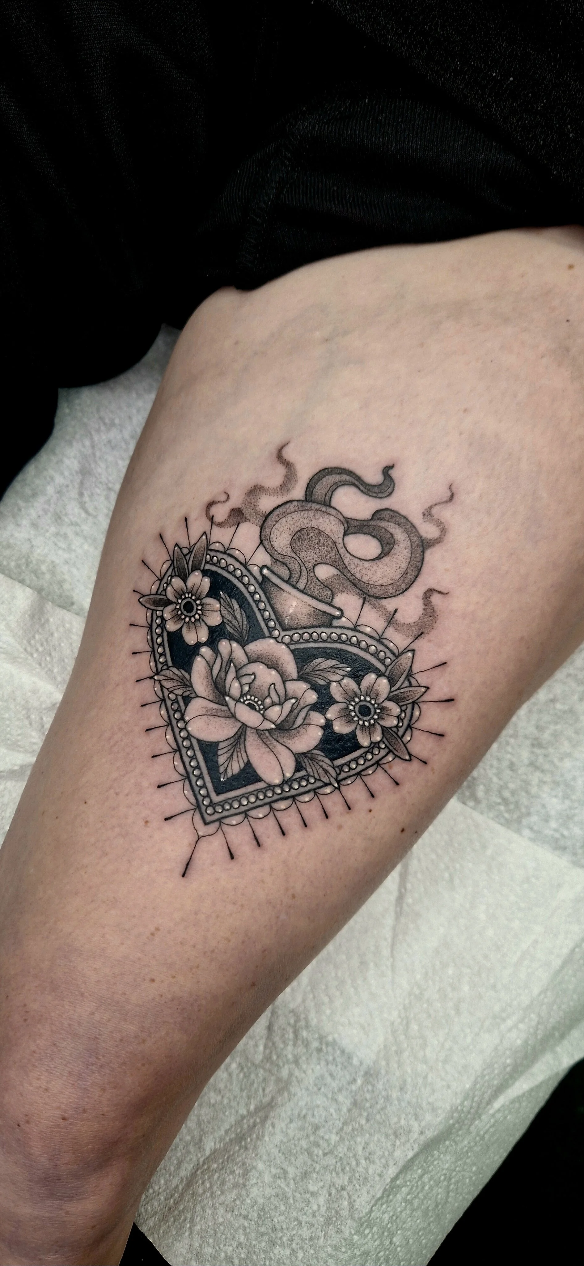Black and grey tattoo of a sacred heart filled with fine line flowers, a bold black background and fine line details.