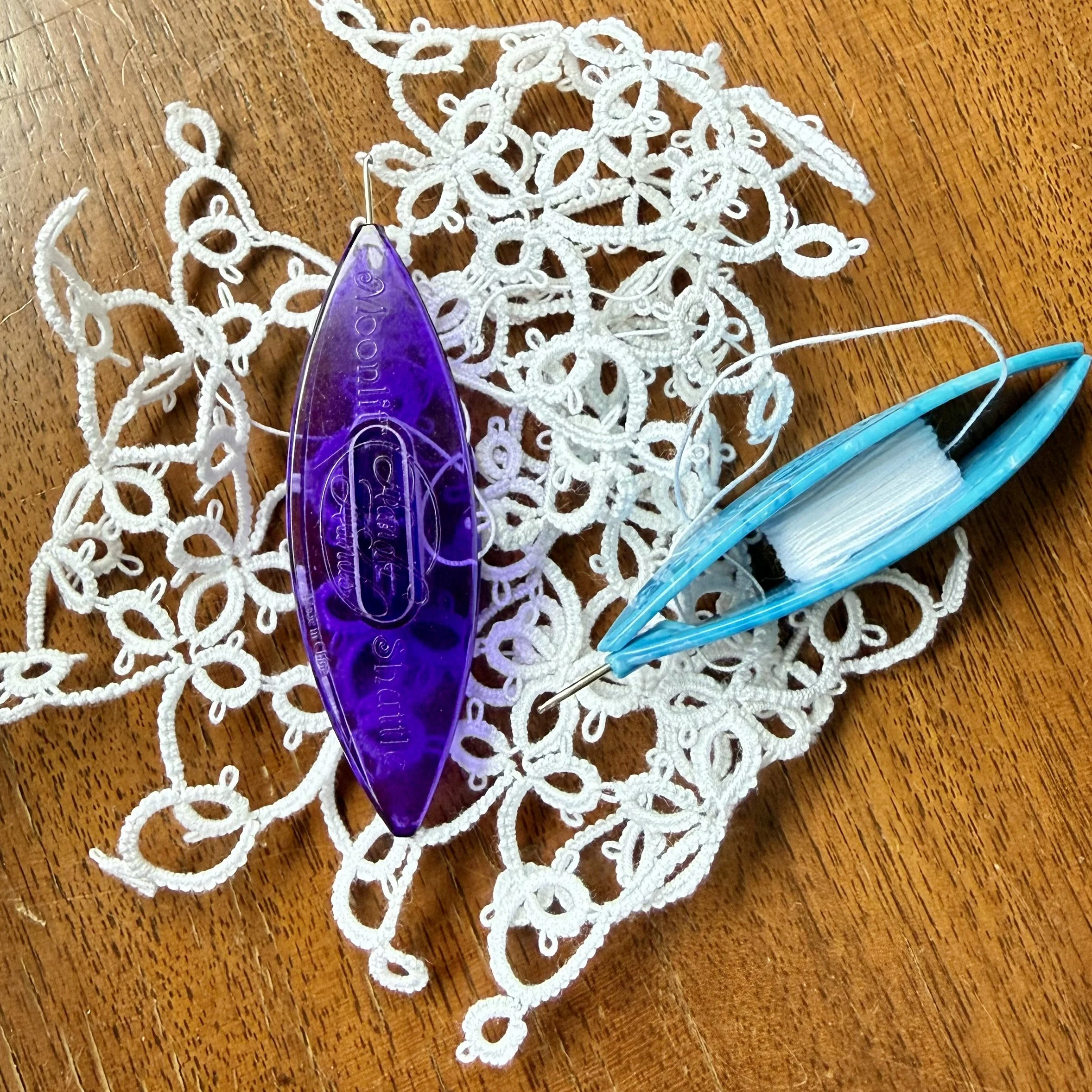 Two hair clips, one purple and one blue, resting on a white lace doily on a wooden surface.