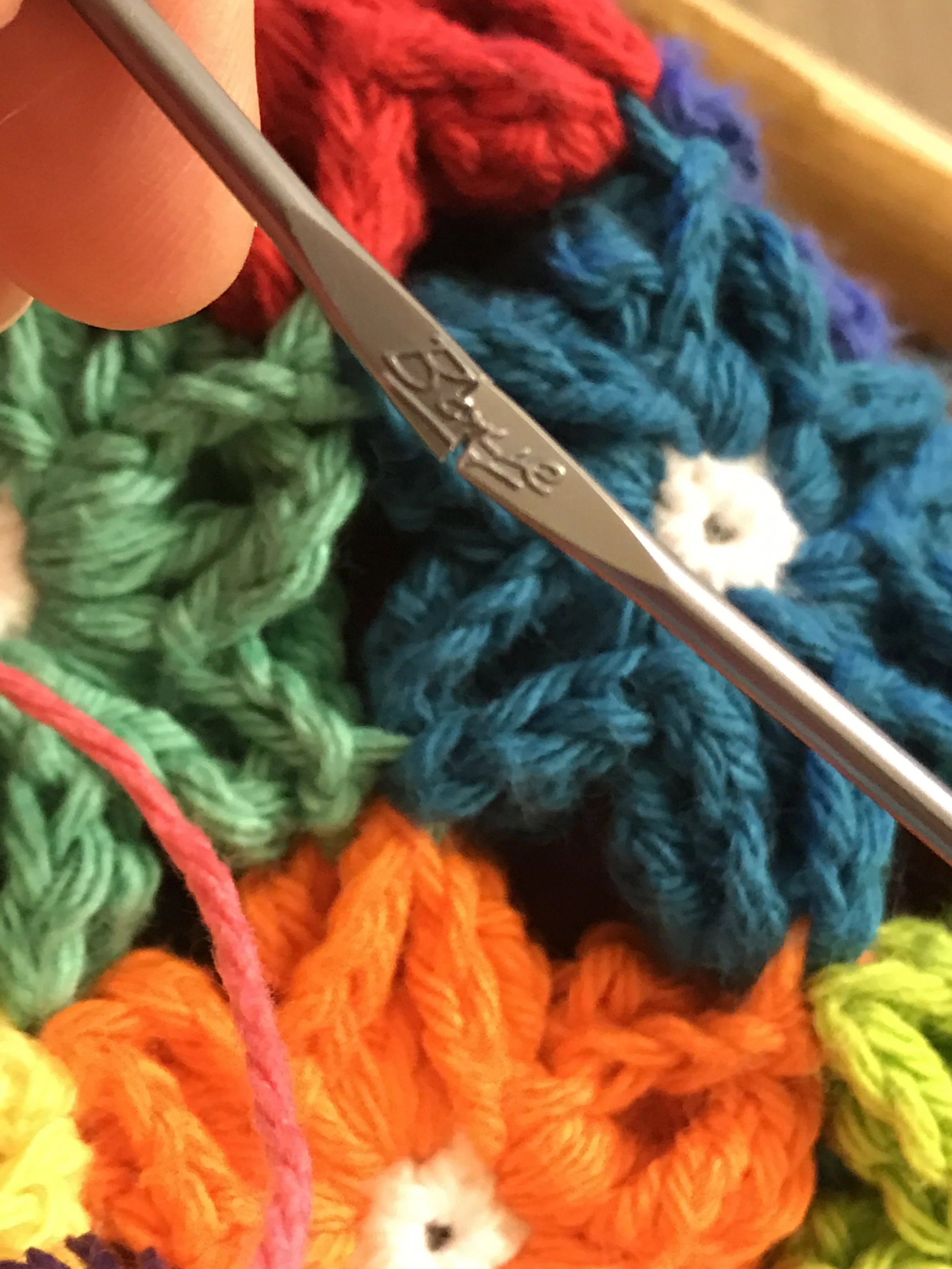 Close-up of colorful crocheted flowers with a knitting crochet hook.