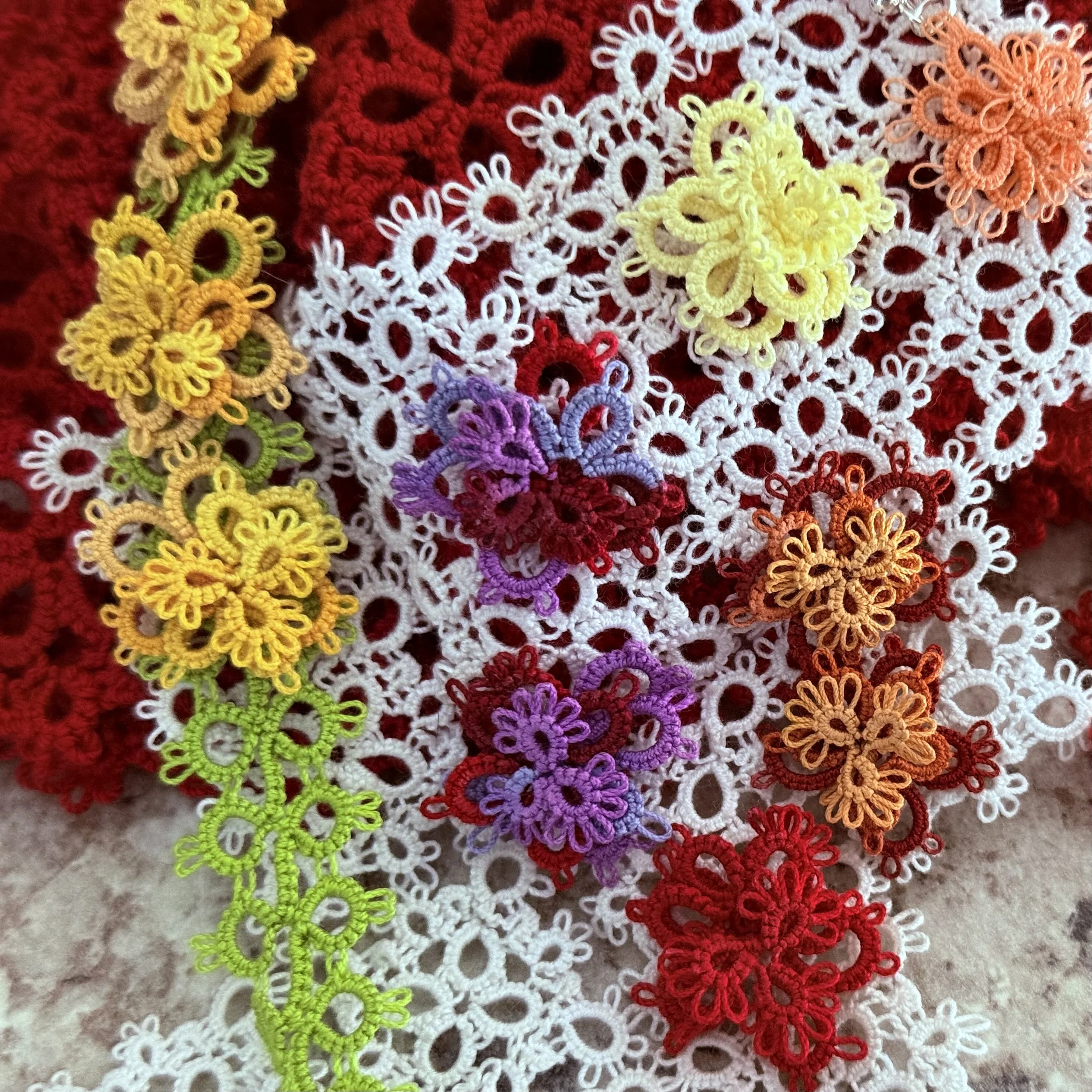 Colorful embroidered floral lace motifs in yellow, purple, red, orange, and white on a red and white lace background.