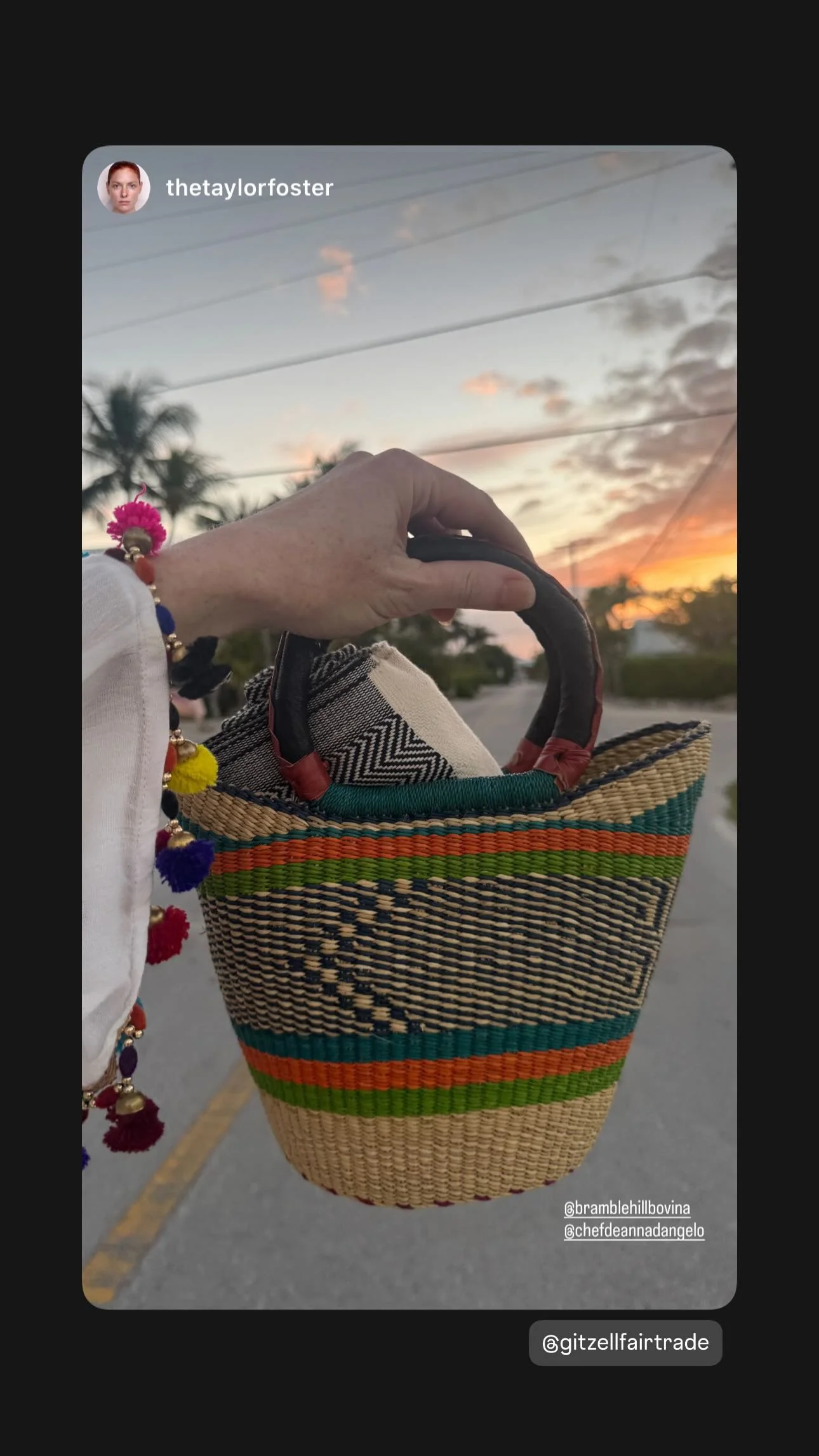 Person holding a colorful woven handcrafted bag during sunset on a quiet street. The person is wearing a white shirt and a colorful bracelet with pom-poms.