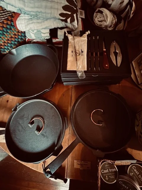 Cast iron cookware set including pots and lids, placed on a wooden surface, with a knife set and kitchen towels nearby.