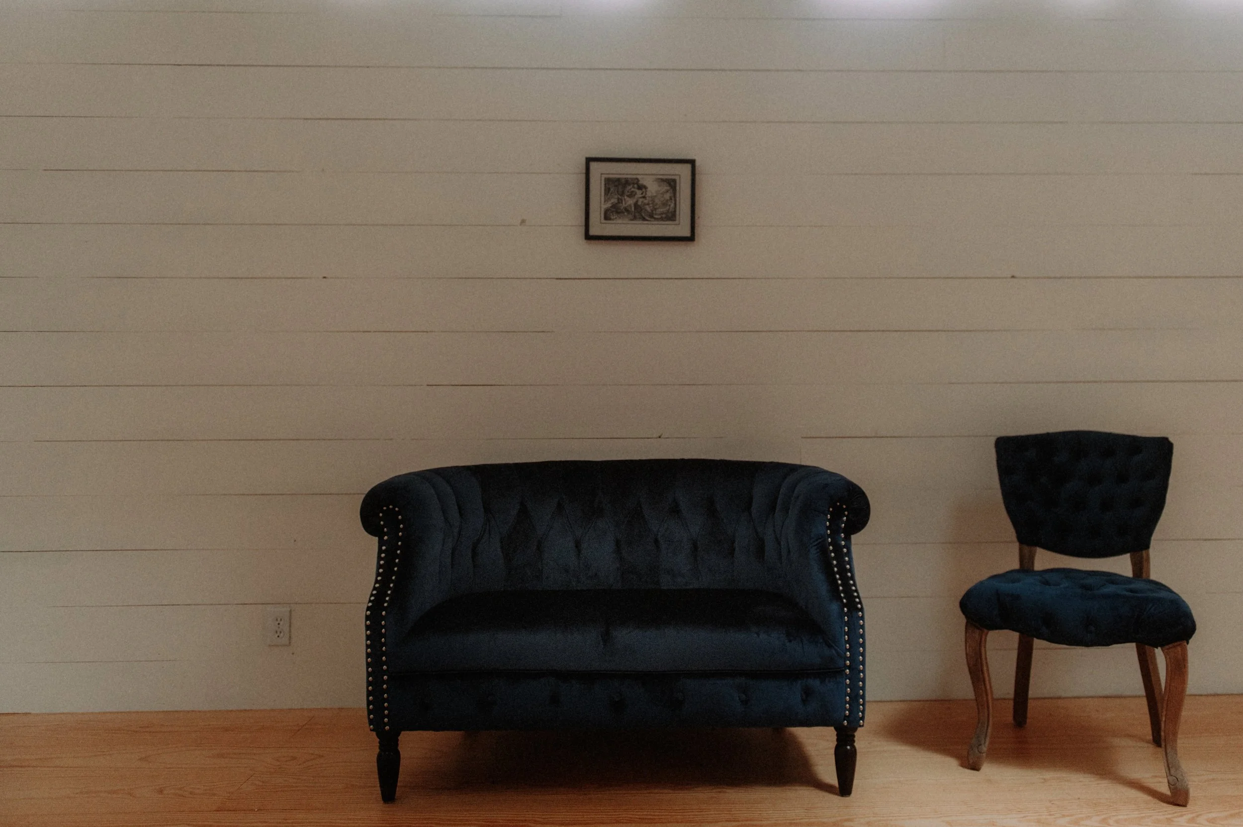 Indoor seating area with a loveseat and chair against a light-colored wall.