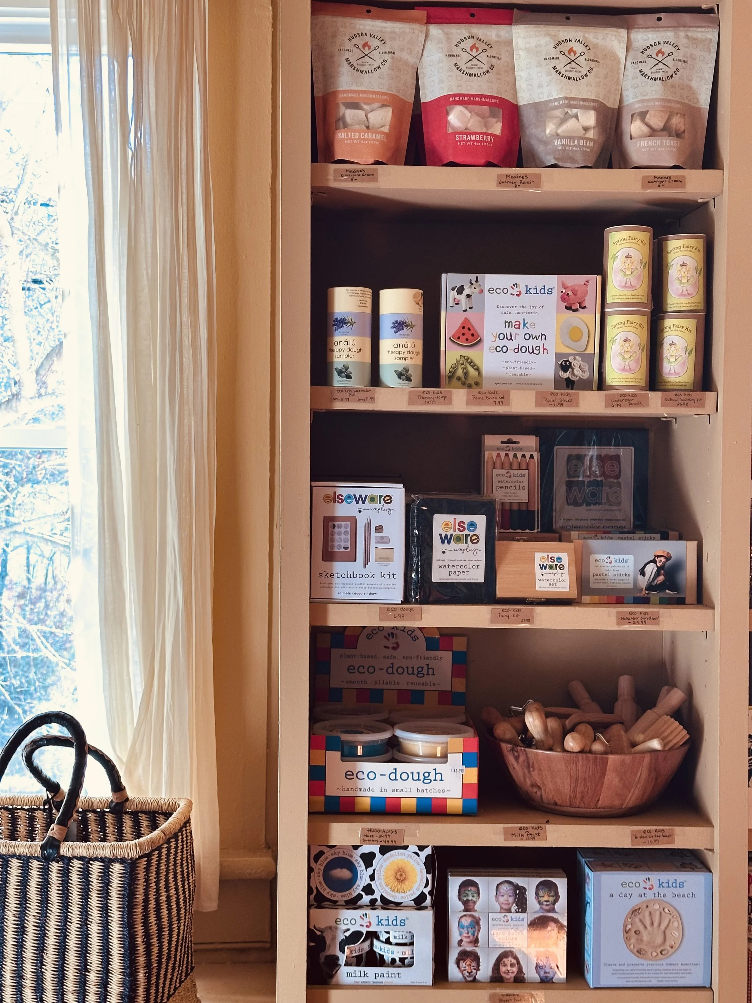 Shelf containing bags of flavored marshmallows, eco-friendly craft kits, watercolors, eco-dough, and face paint sets for kids.