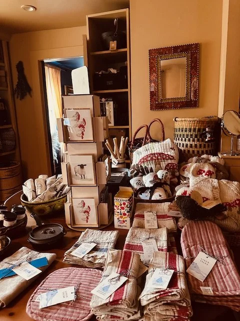 Table filled with folded shopping items, including towels, gloves, and plush toys, surrounded by miscellaneous household items.