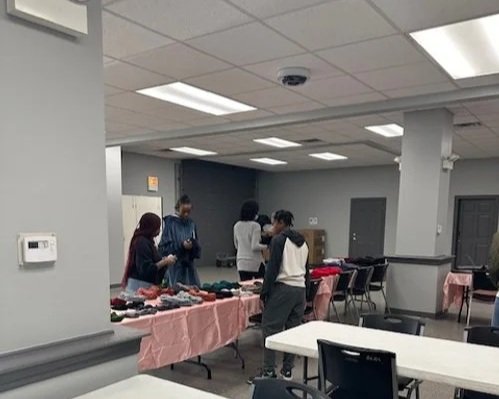 People shopping at a market stall inside a room with pink tablecloths and chairs.