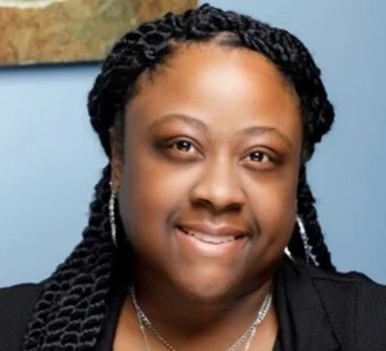 Close-up of a smiling Black woman with braided hair, wearing earrings and a necklace.