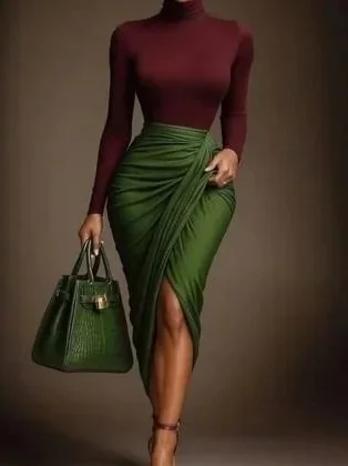 Woman wearing a maroon turtleneck top and green high-slit skirt, holding a green handbag and wearing high heels.