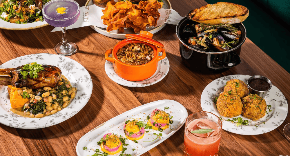 Variety of Indian dishes on a wooden table including lentil soup, fried snacks, seafood, vegetable curry, and drinks.