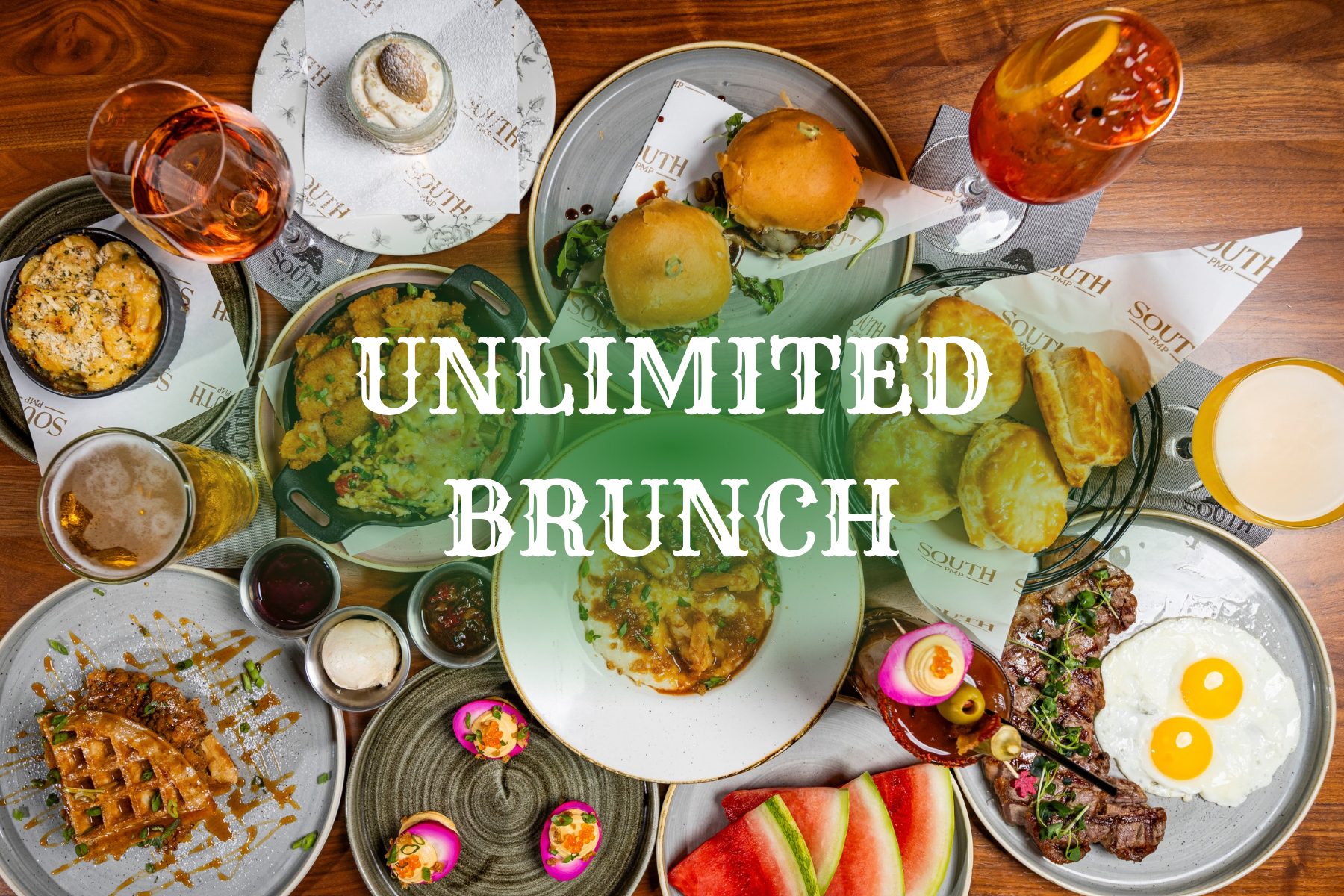 Overhead view of a brunch table with waffles, eggs, steak, biscuits, sliders, watermelon, and drinks. White text reads ‘Unlimited Brunch.’