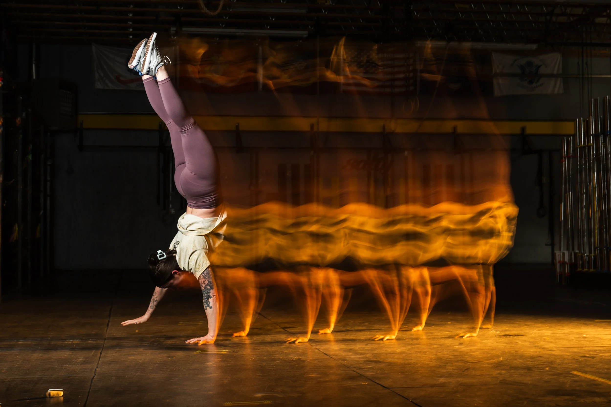 A person performing a handstand in a gym, with flames and fire effects edited into the background to create a fiery appearance.