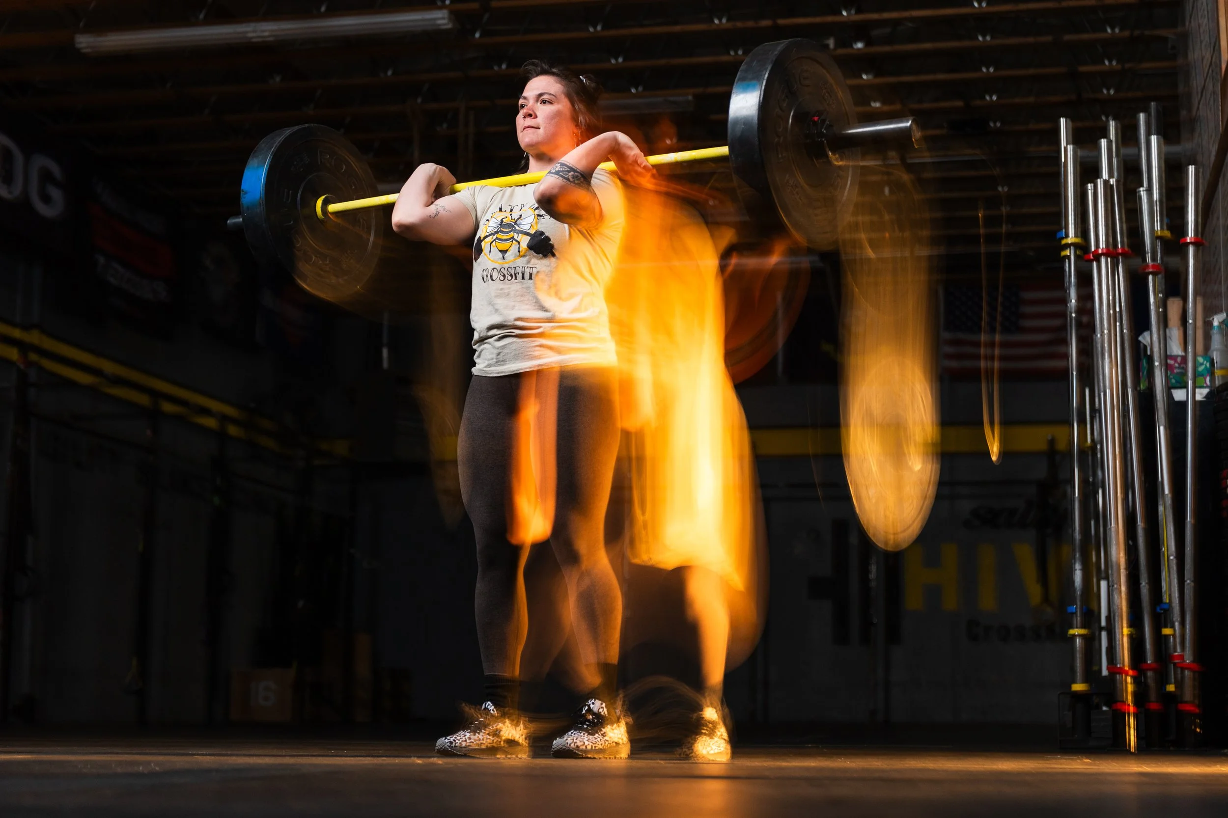 A woman in workout clothes lifting a barbell to her shoulders in a gym, with flames on her shoes and a blurred motion effect.