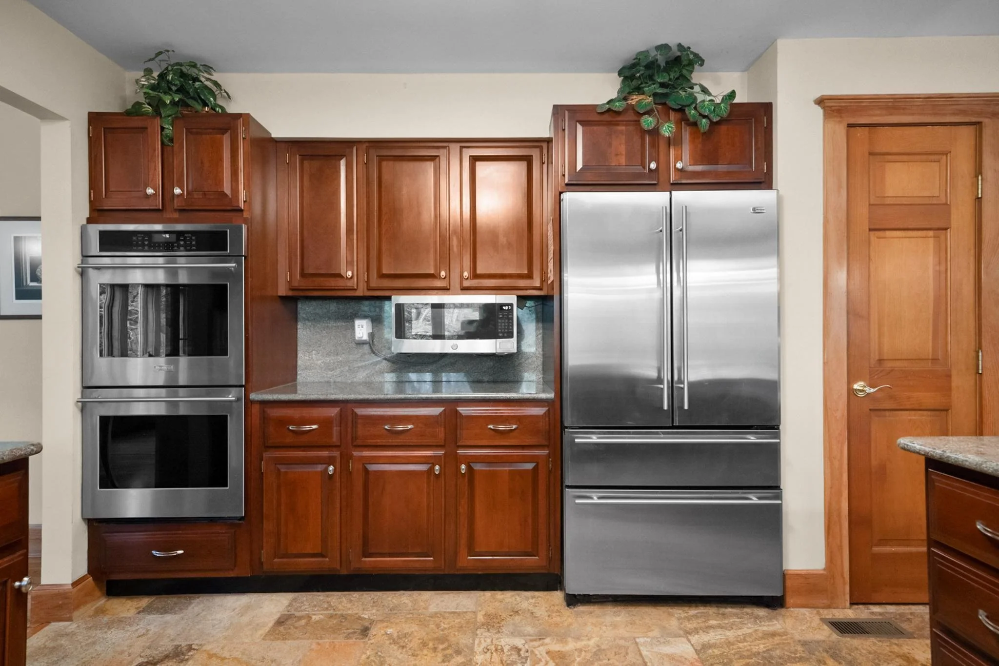 Kitchen with wooden cabinets, stainless steel refrigerator and oven, microwave, and granite countertops.