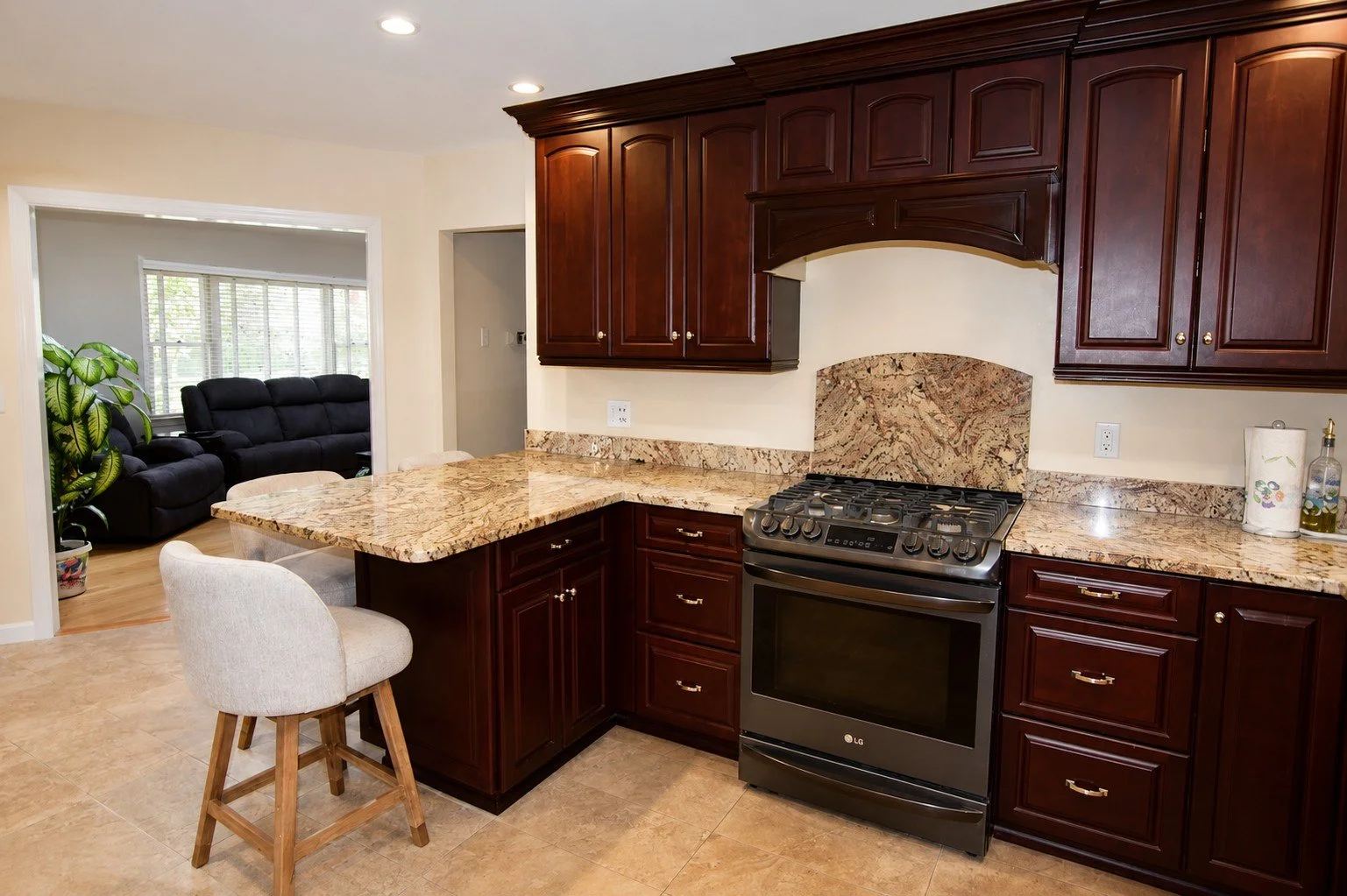 Kitchen with dark wood cabinets, granite countertops, and a stainless steel stove, with a living room visible through an open doorway.