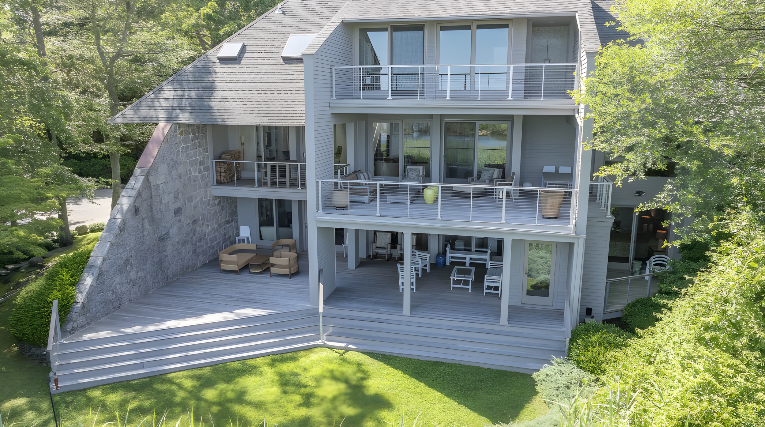 A multi-story house with a large wooden deck and balcony, surrounded by trees and greenery.