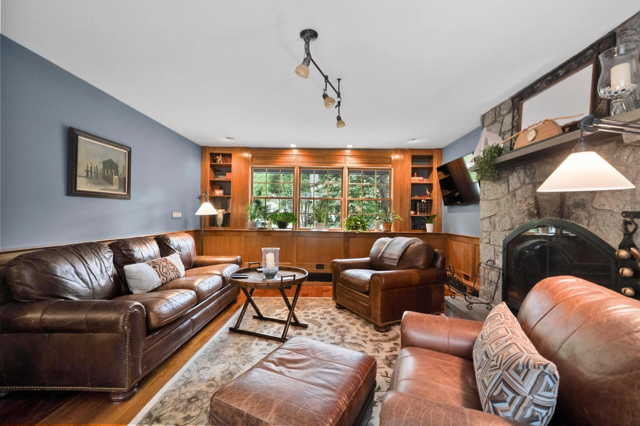 Living room with leather sofas, a large window with wooden framing, a stone fireplace, and decorative items.