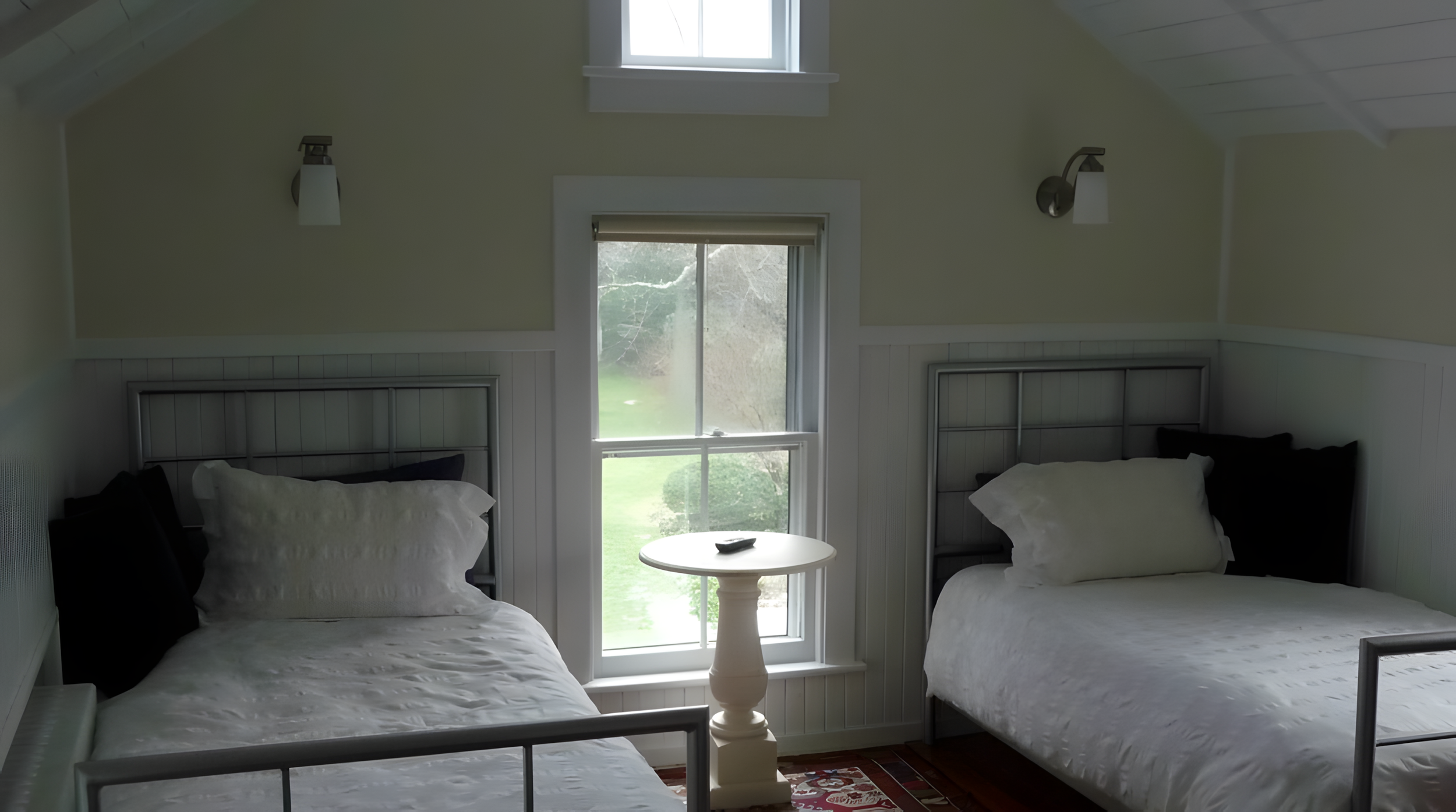 A bedroom with two beds, a small round table between them, and a window showing an outdoor view.