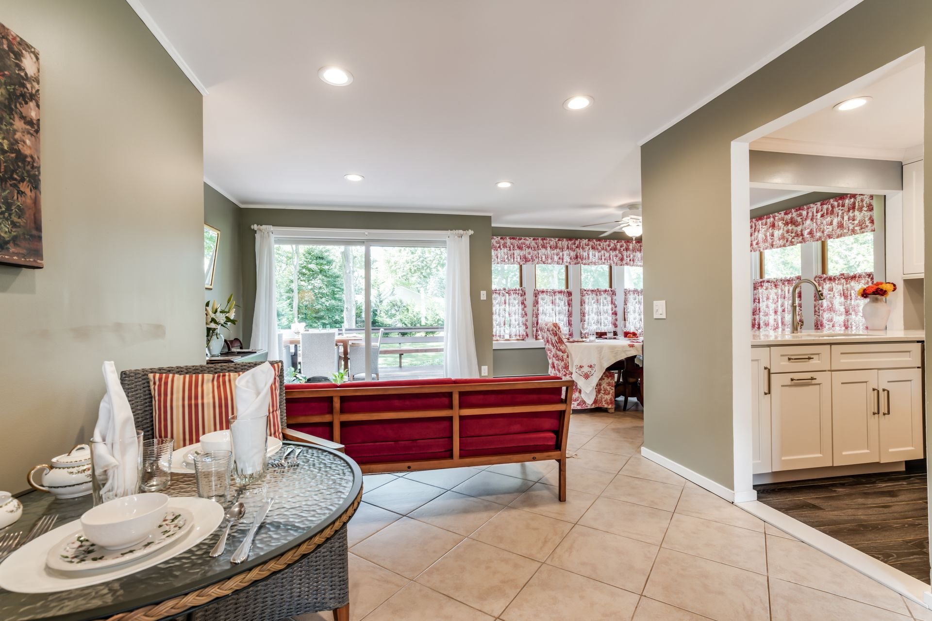 Open-concept living and dining area with view of kitchen, large window, red patterned curtains, and outdoor patio.