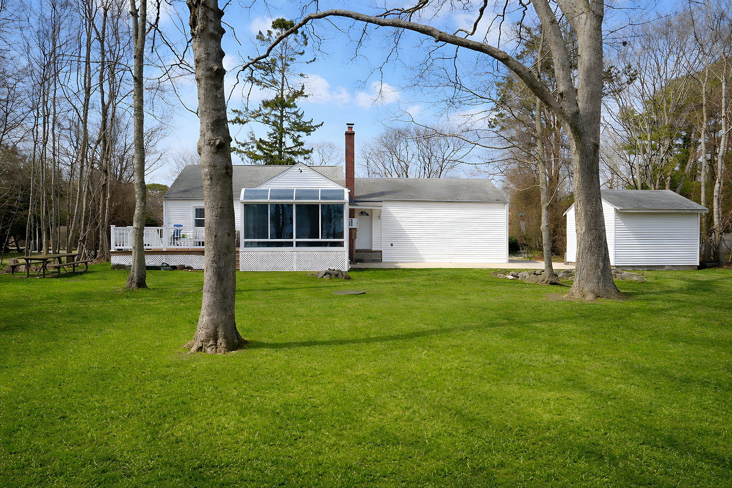 Backyard with green grass, several trees, and a white house with a screened porch and attached Garage.