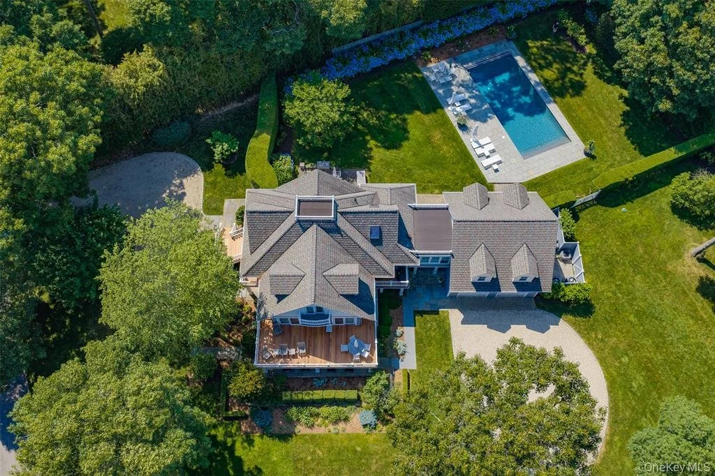 An aerial view of a large house with a gray roof, a backyard with a swimming pool, and surrounding green trees and lawn.