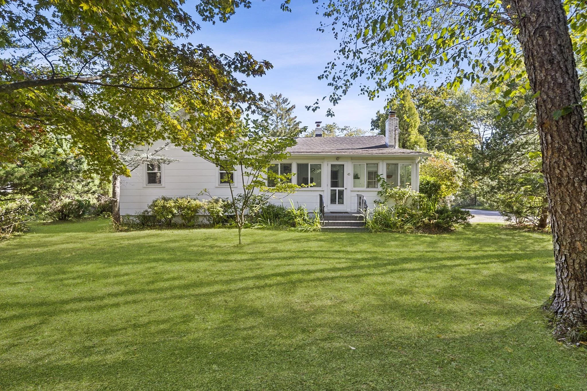 A white house with a porch, surrounded by green trees and a well-maintained lawn on a sunny day.