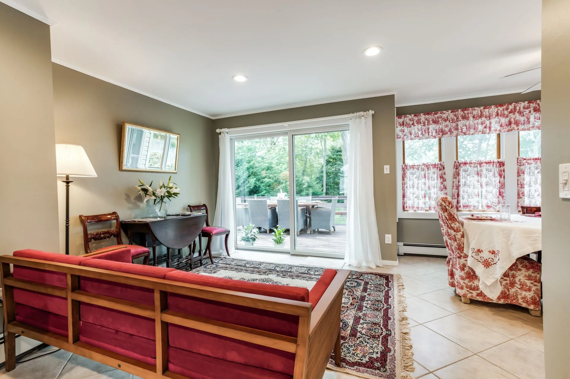 Living room with sliding glass door leading to outdoor deck, dining area with red floral curtains, and sofa with red cushions.