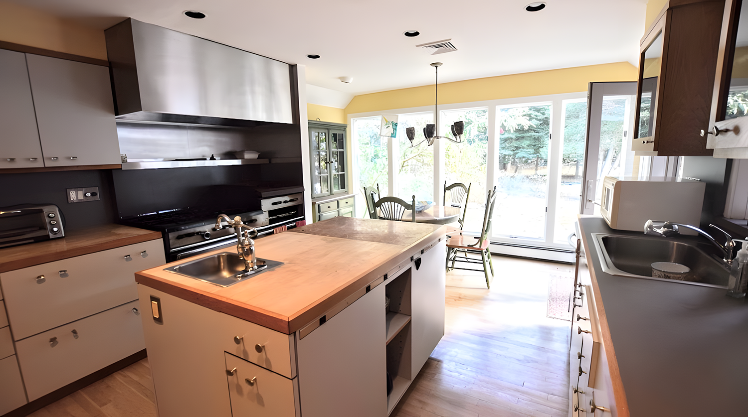 Bright kitchen with wooden countertops, white cabinets, stainless steel appliances, and a dining area with large windows and sliding glass doors leading outside