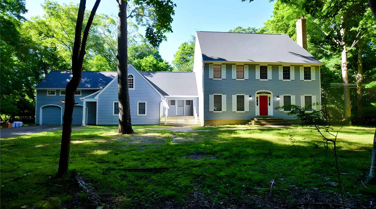 A large blue house with a natty gray roof, several windows, and a red front door, surrounded by green trees and a grassy yard.