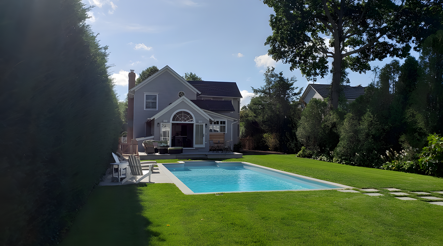 Kitchen with white island counter, black cabinets, and view of backyard with pool, lounge chairs, and green trees.