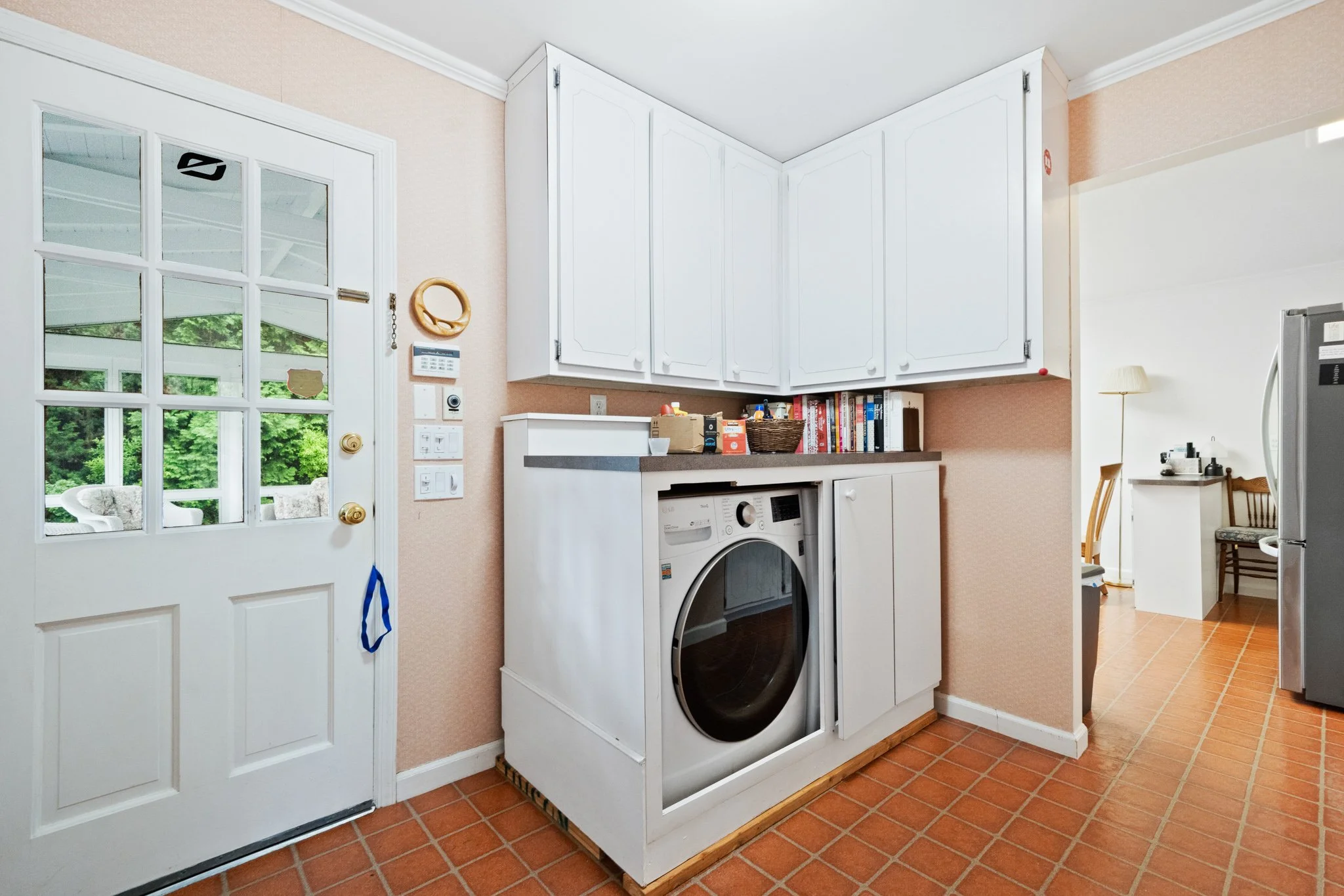 Kitchen with white cabinets, washing machine, refrigerator, and a door with glass panes showing outdoor greenery.