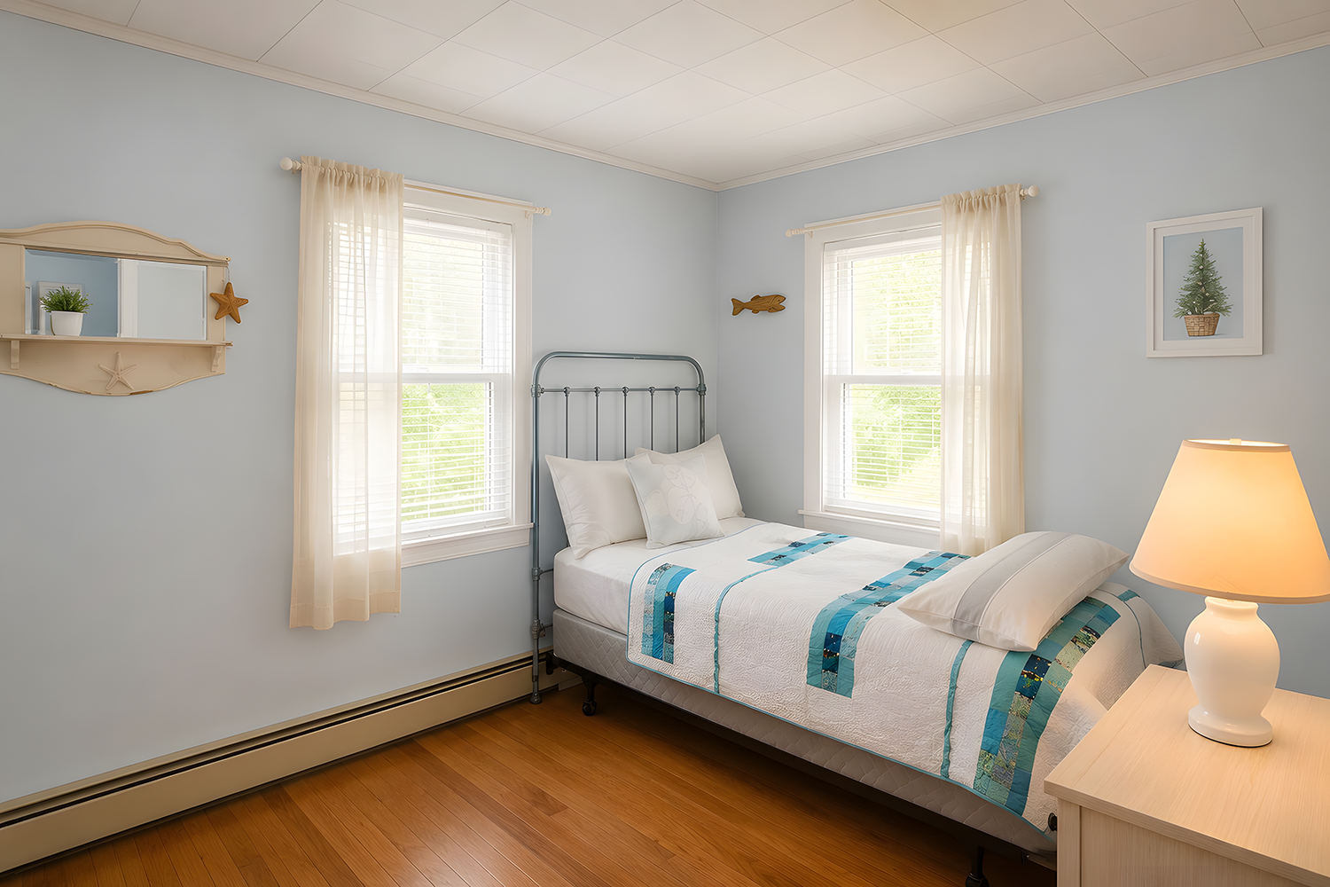 A cozy bedroom with light blue walls, two windows with white blinds and curtains, a metal bed with white and blue bedding, a wooden nightstand with a table lamp, and wall decorations including framed pictures and wooden fish.