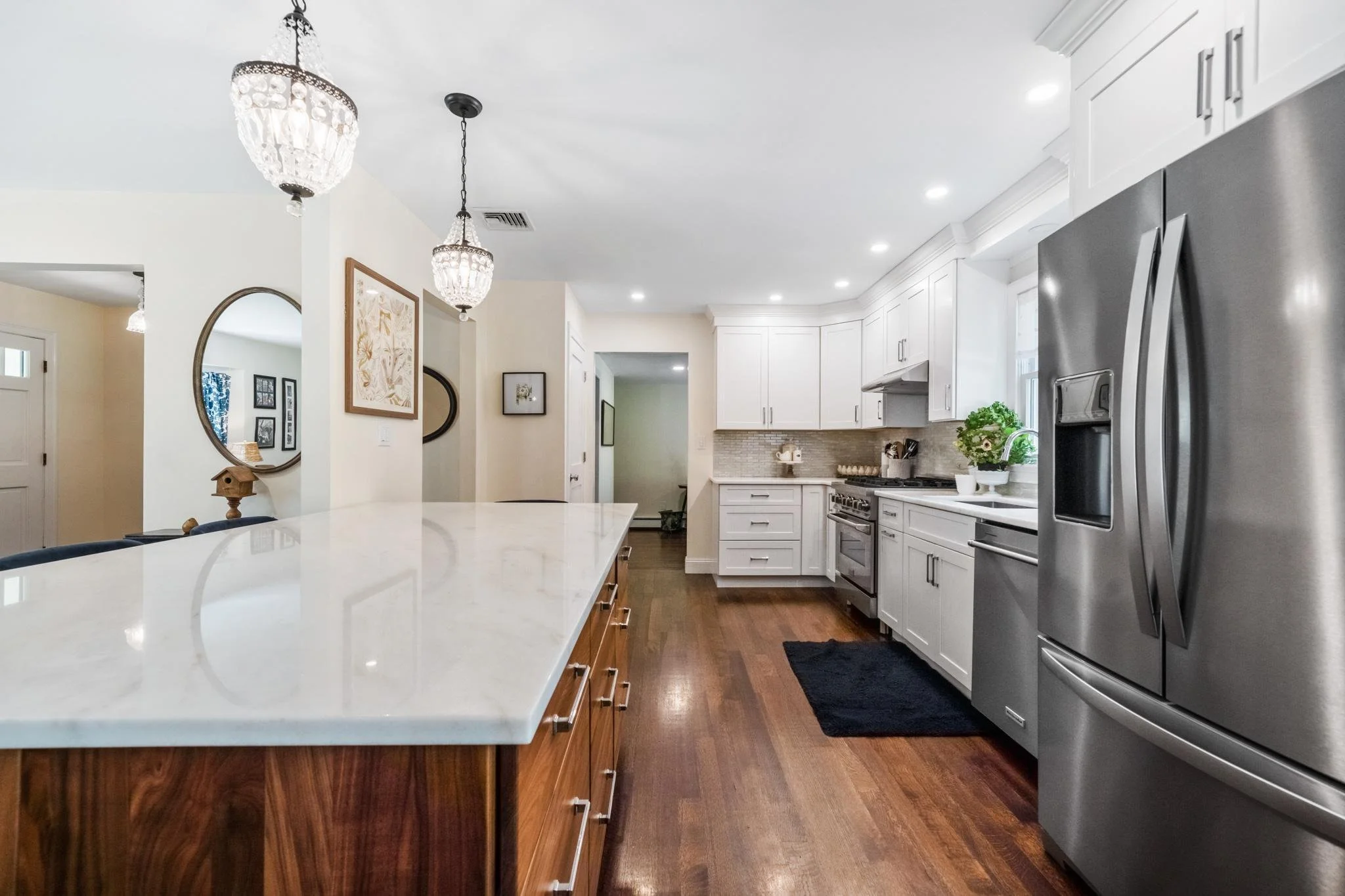 Modern kitchen with white cabinets, stainless steel refrigerator, hardwood floors, and decorative lighting fixtures.
